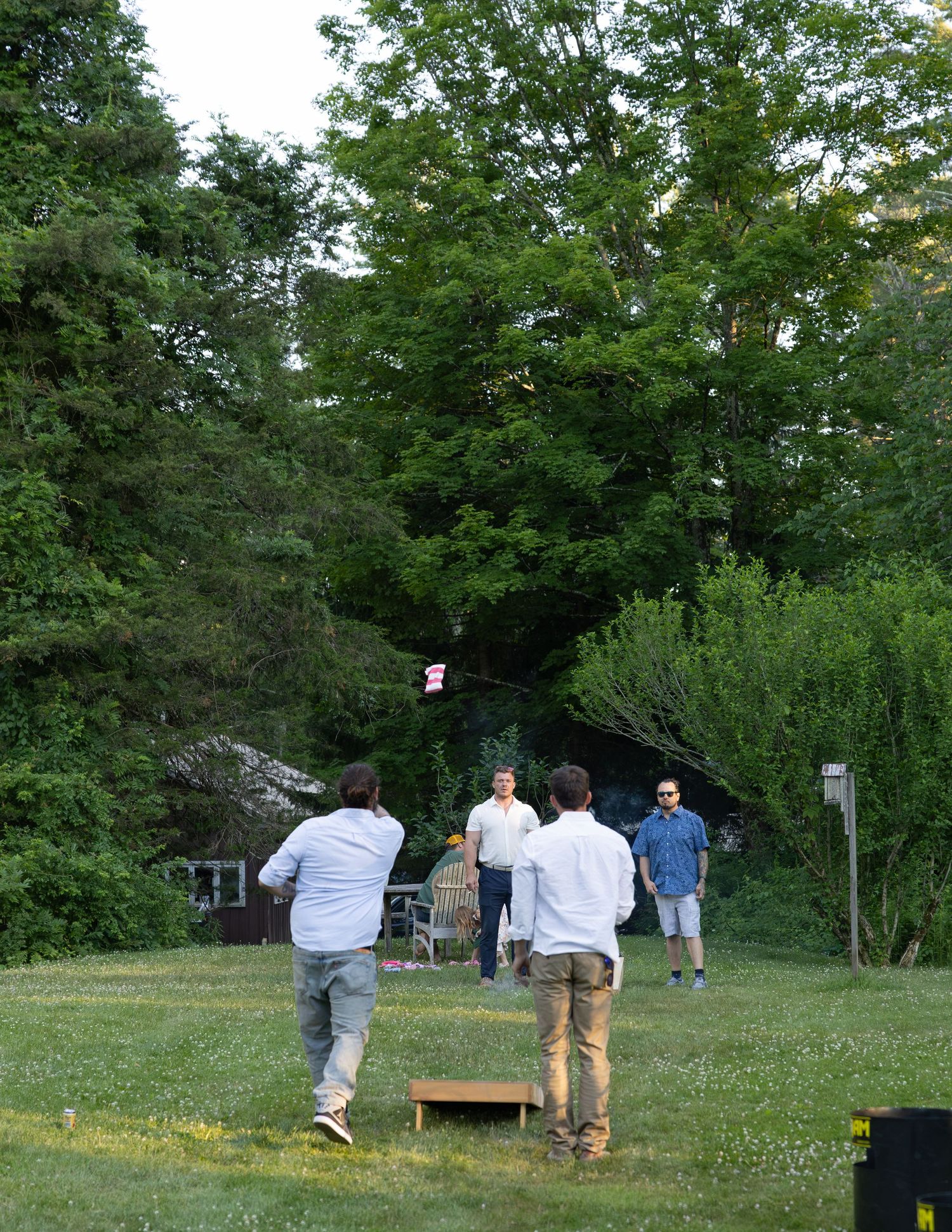 Group of men playing cornhole on a green lawn during an outdoor backyard wedding reception.