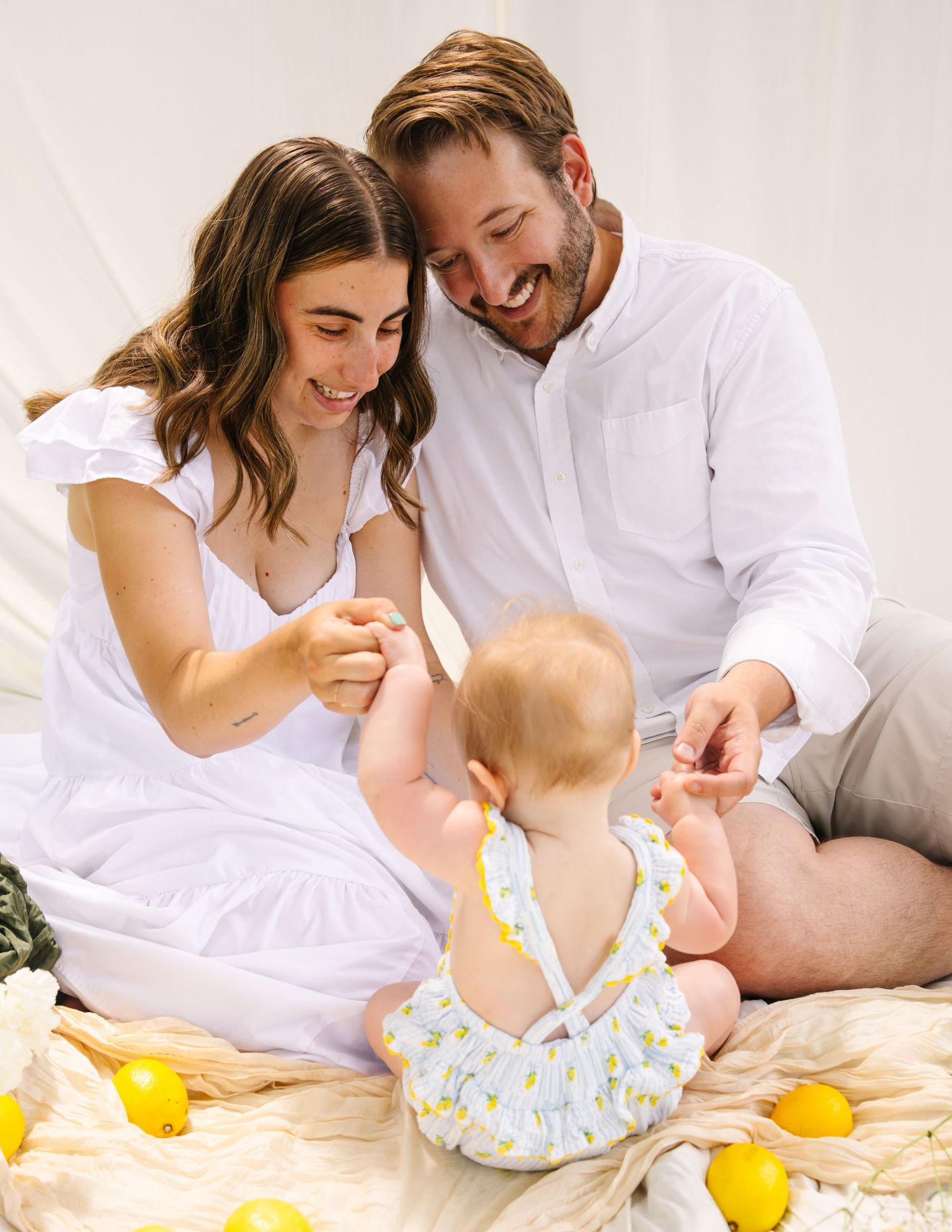 Happy young parents smiling and playing with their baby girl surrounded by lemons indoors.