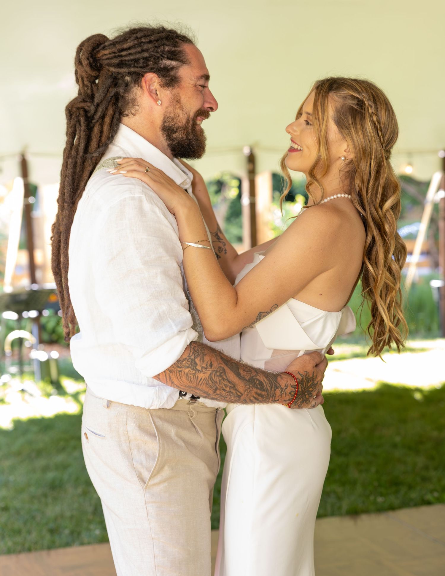 Couple in white wedding attire embracing and smiling at each other during outdoor celebration.