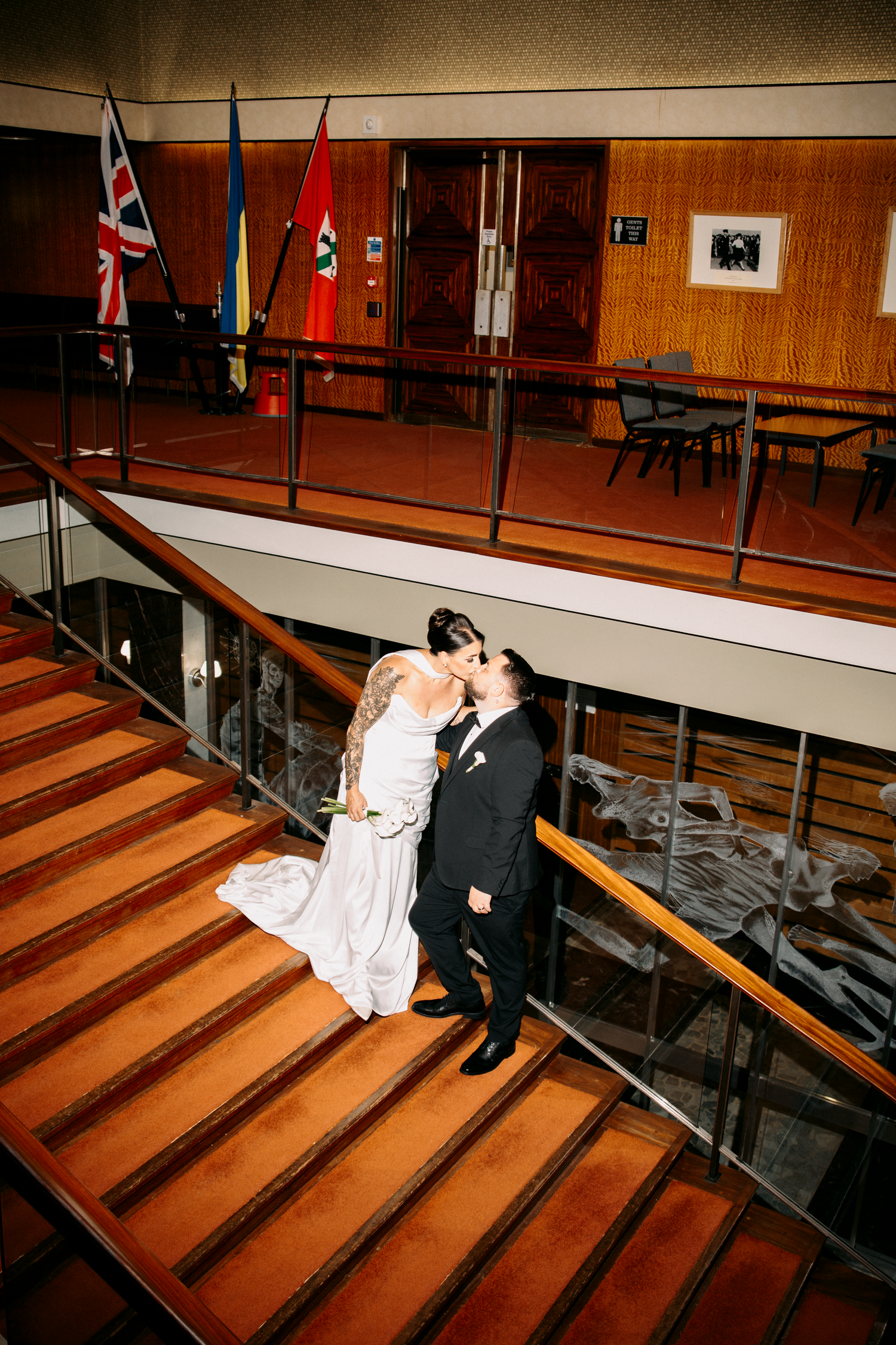 Bride and groom share a romantic kiss on wooden stairs with flags displayed in the background.