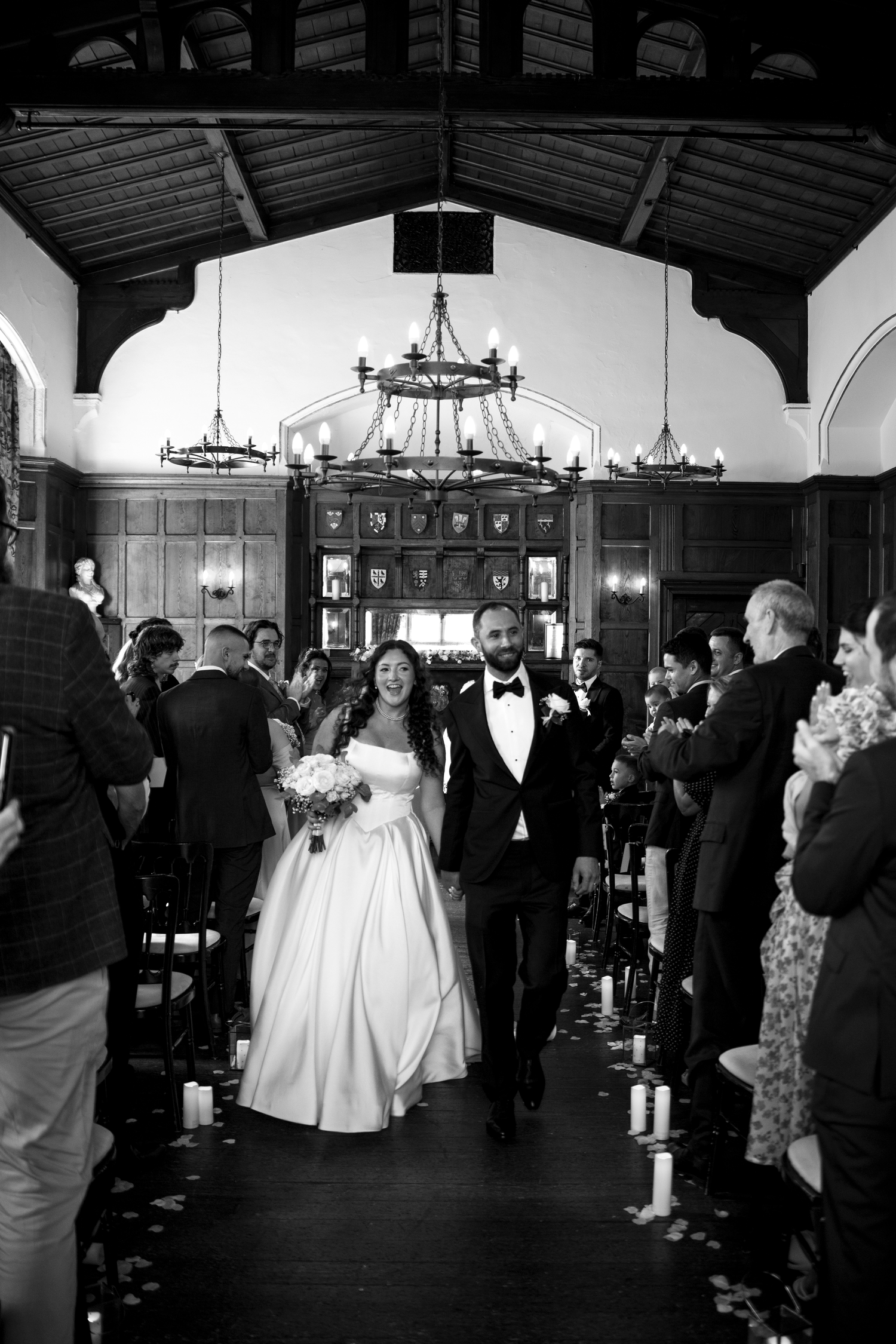 Black and white photo of a bride and groom walking down the aisle after their wedding ceremony in an elegant venue.