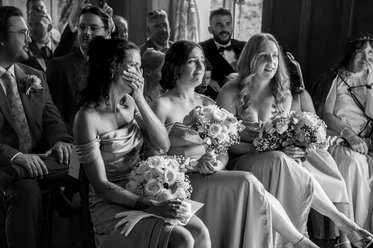 Black and white photo of emotional bridesmaids crying and holding bouquets during a wedding ceremony.