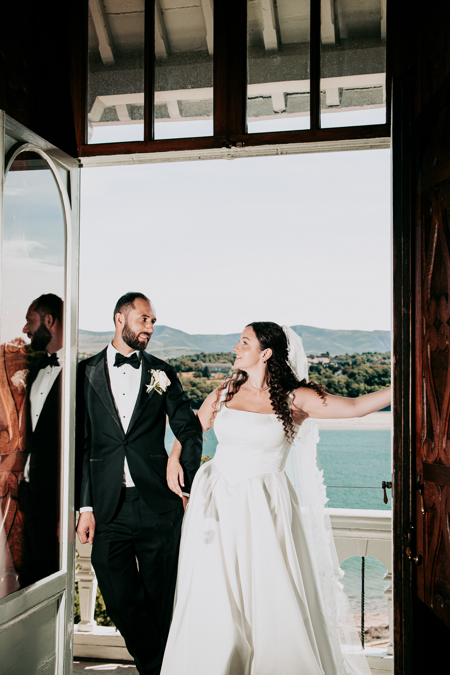 Bride and groom share a joyful moment in an open doorway with scenic lake and mountain views behind them.