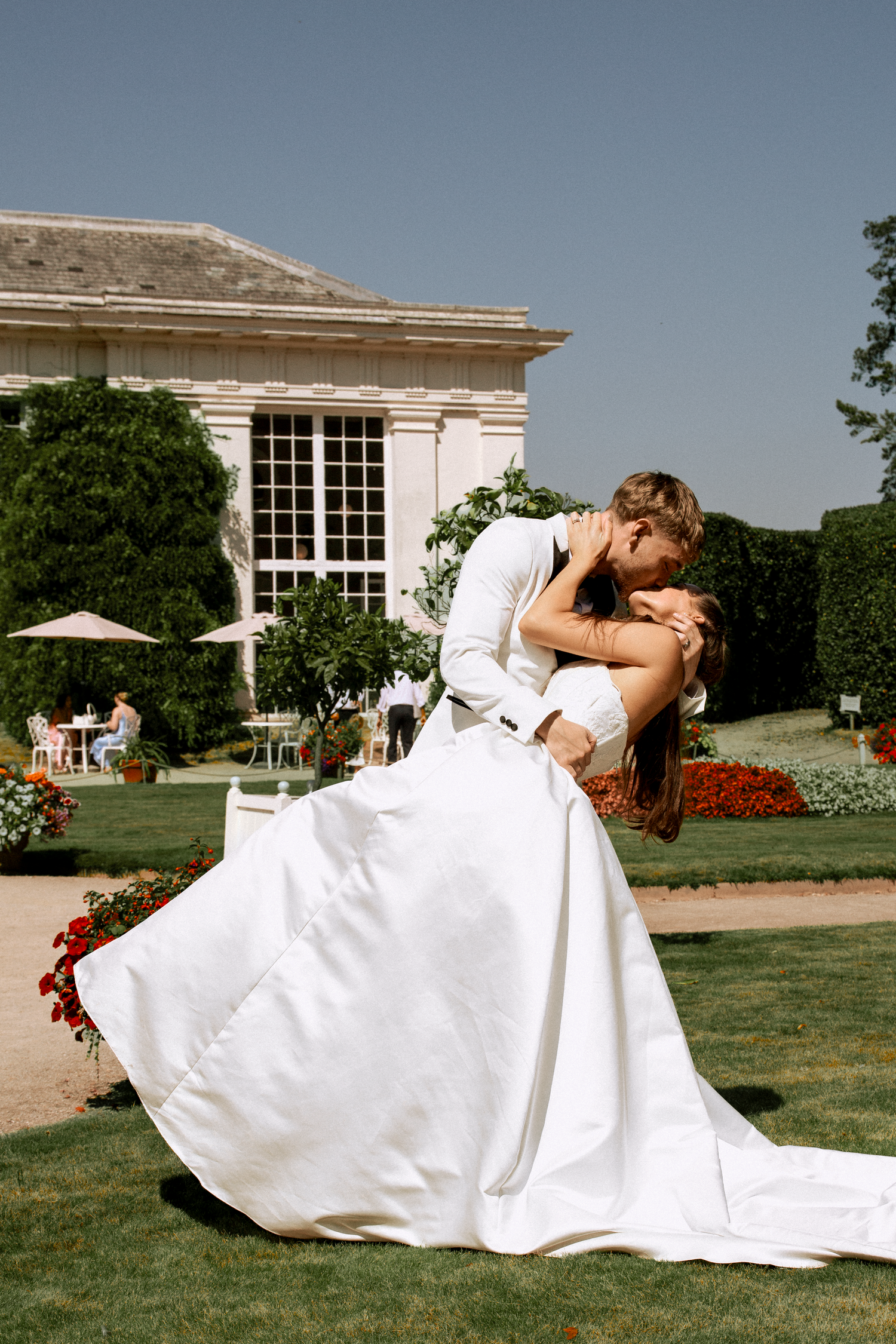 Groom dips bride for a romantic kiss in a formal garden outside an elegant estate.