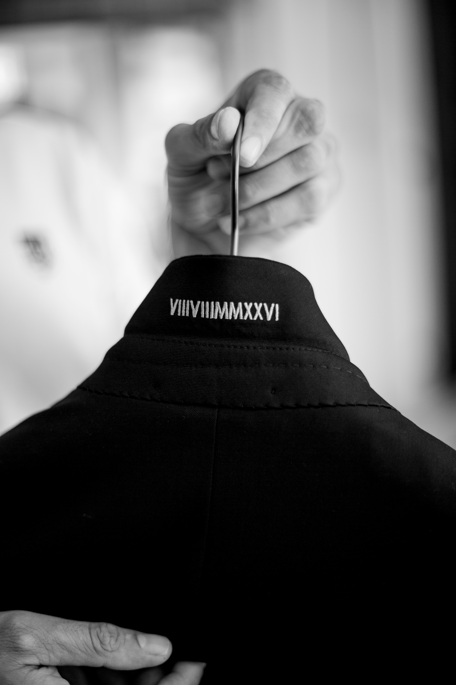 Black jacket collar with Roman numerals VIIIVIIIMMXXVI embroidered in white, held on a hanger in black and white photo.