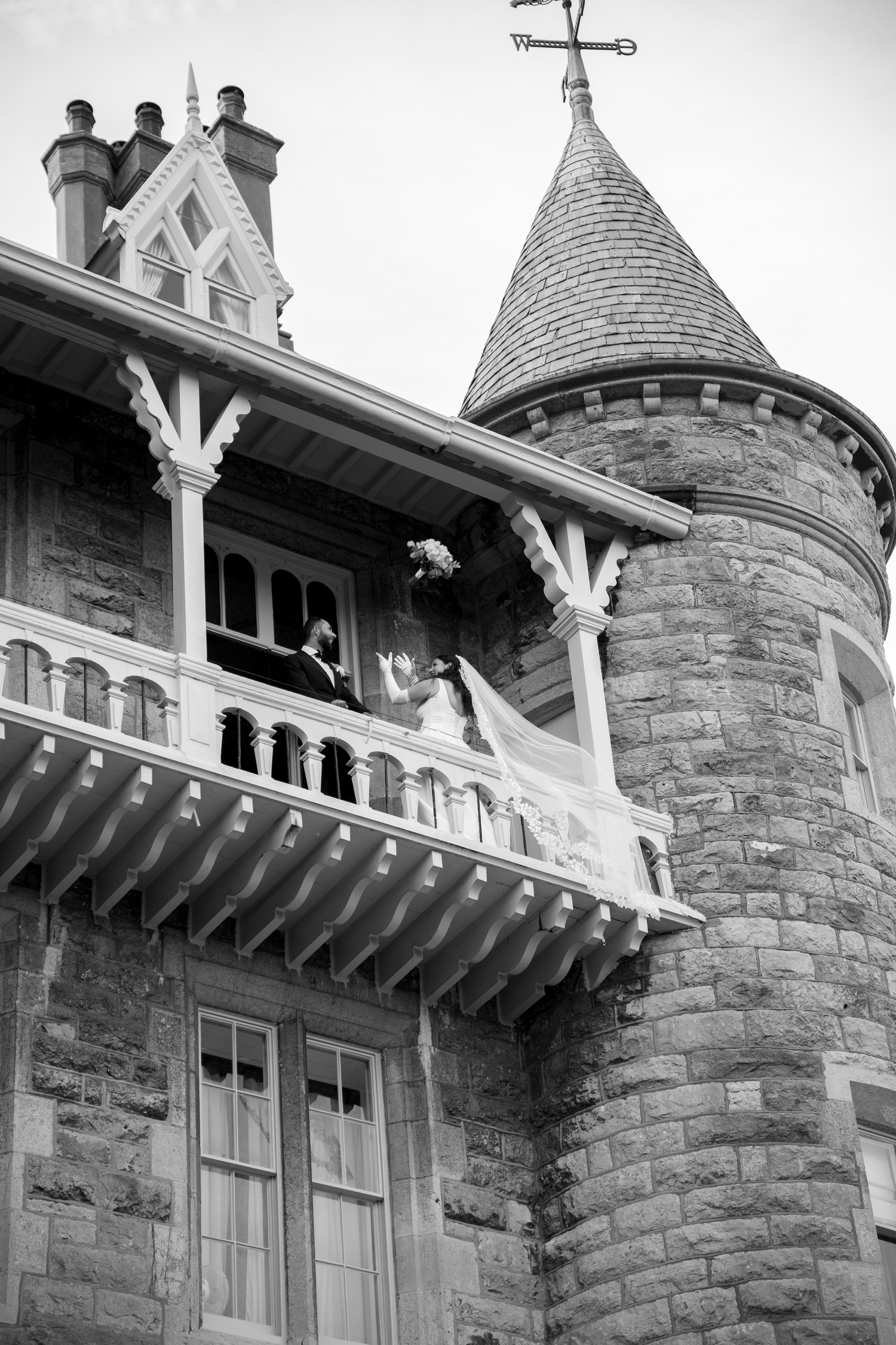 Bride and groom on castle balcony with turret in black and white wedding photo.