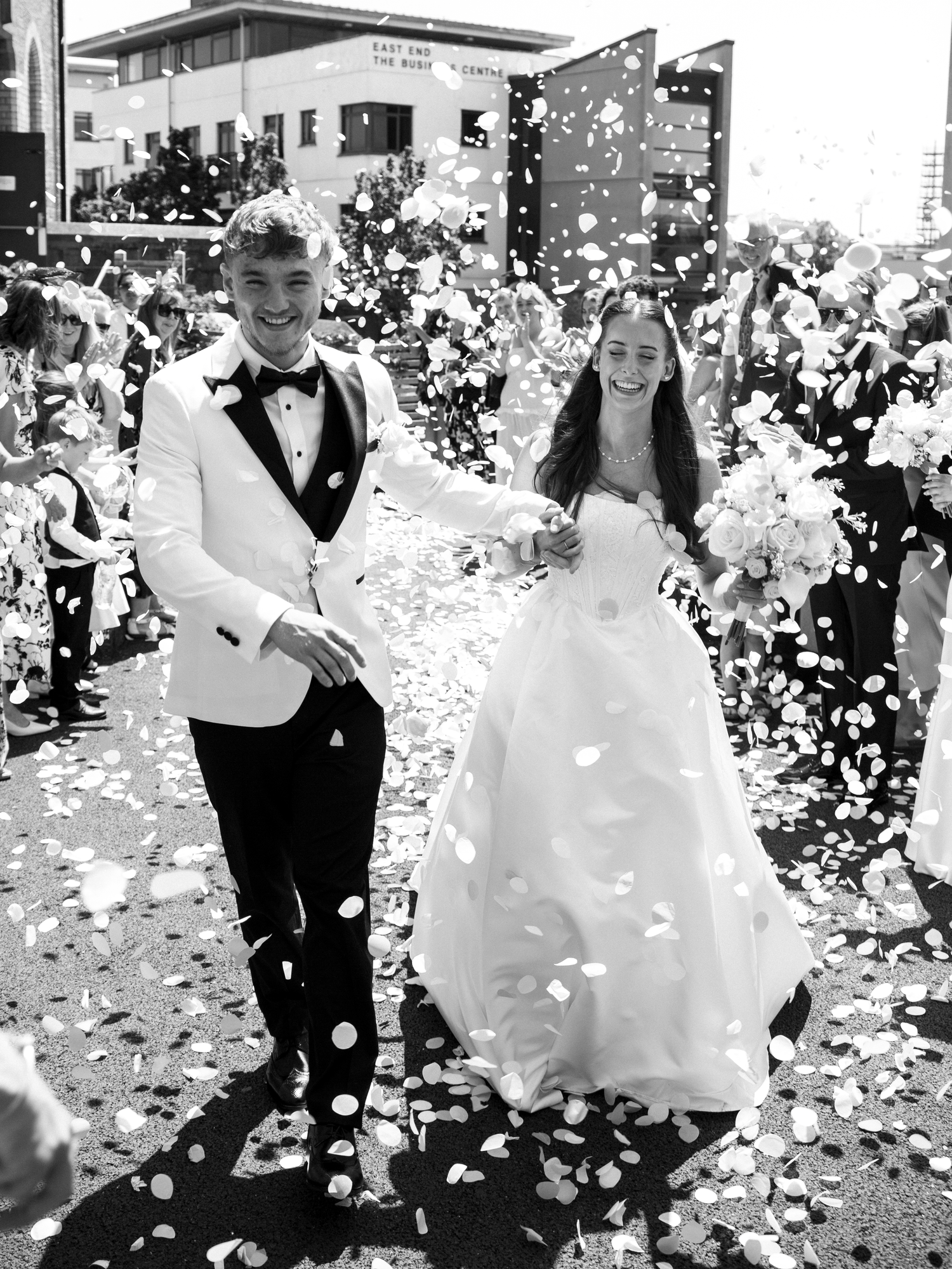 Bride and groom walking through confetti shower after wedding ceremony in black and white photo.