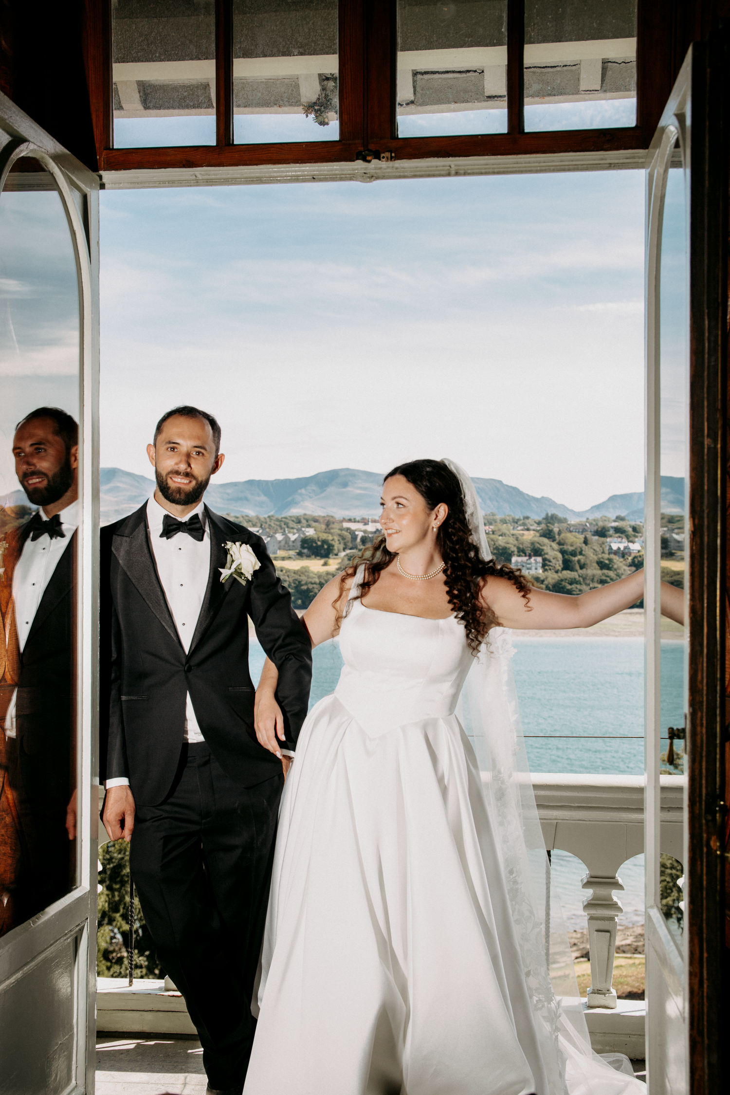 Bride and groom stand in open French doors with scenic mountain and ocean views on their wedding day.