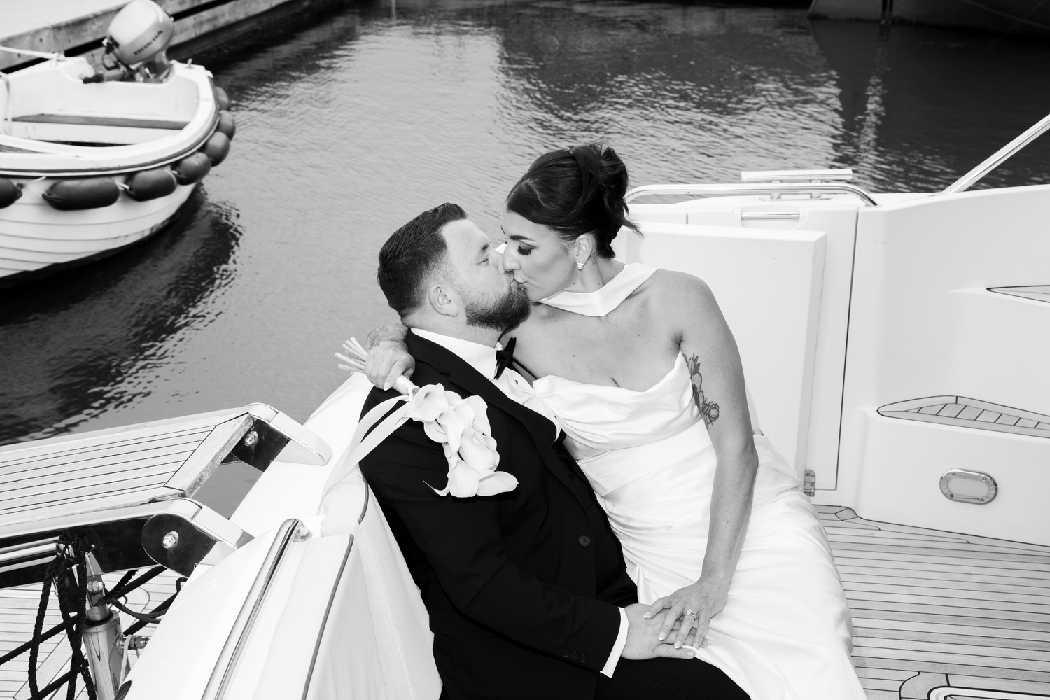 Black and white photo of bride and groom sharing a romantic kiss while seated on a yacht.