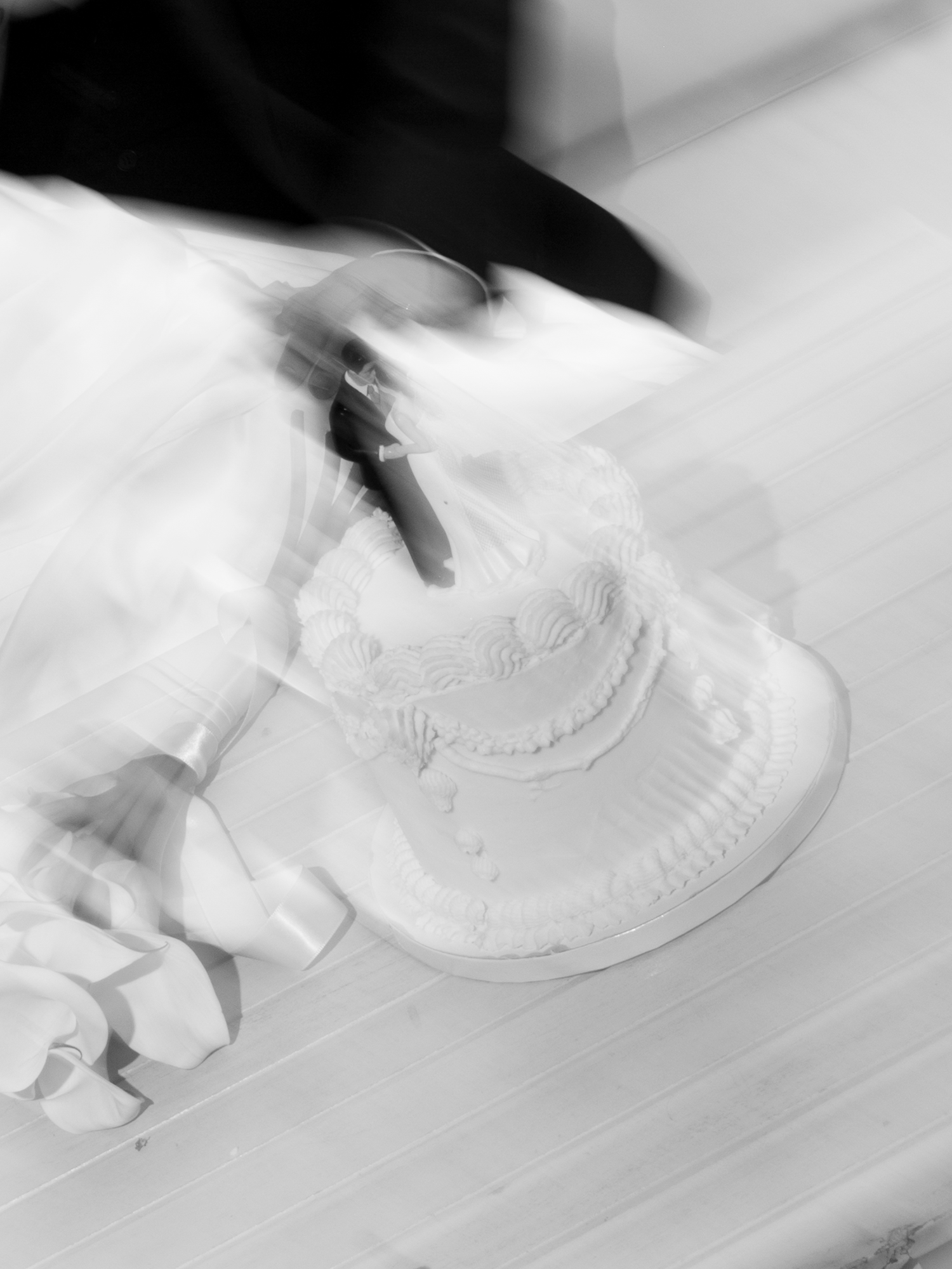Artistic blurred black and white close-up of wedding cake being cut with a knife on a table.