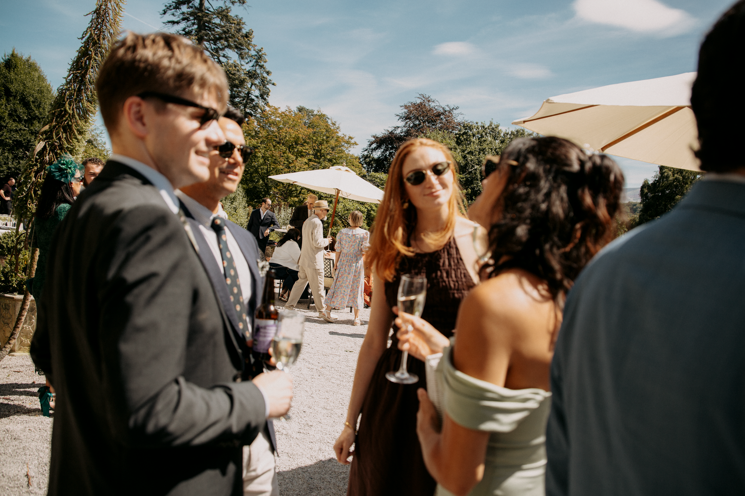 Guests socializing outdoors at a wedding reception, holding champagne glasses in a sunny garden setting.