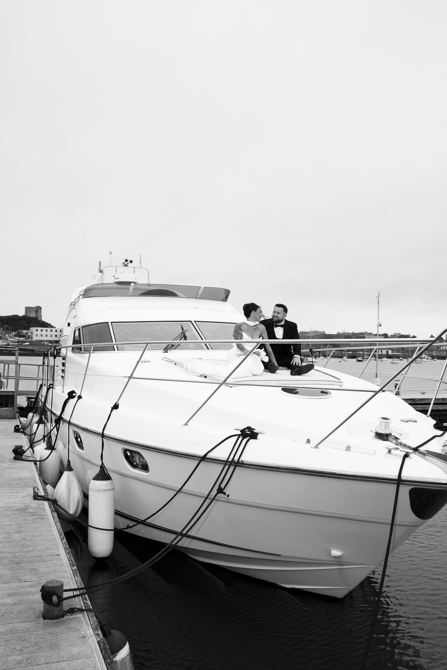 Bride and groom kissing on the bow of a white luxury yacht docked at a marina, black and white photo.