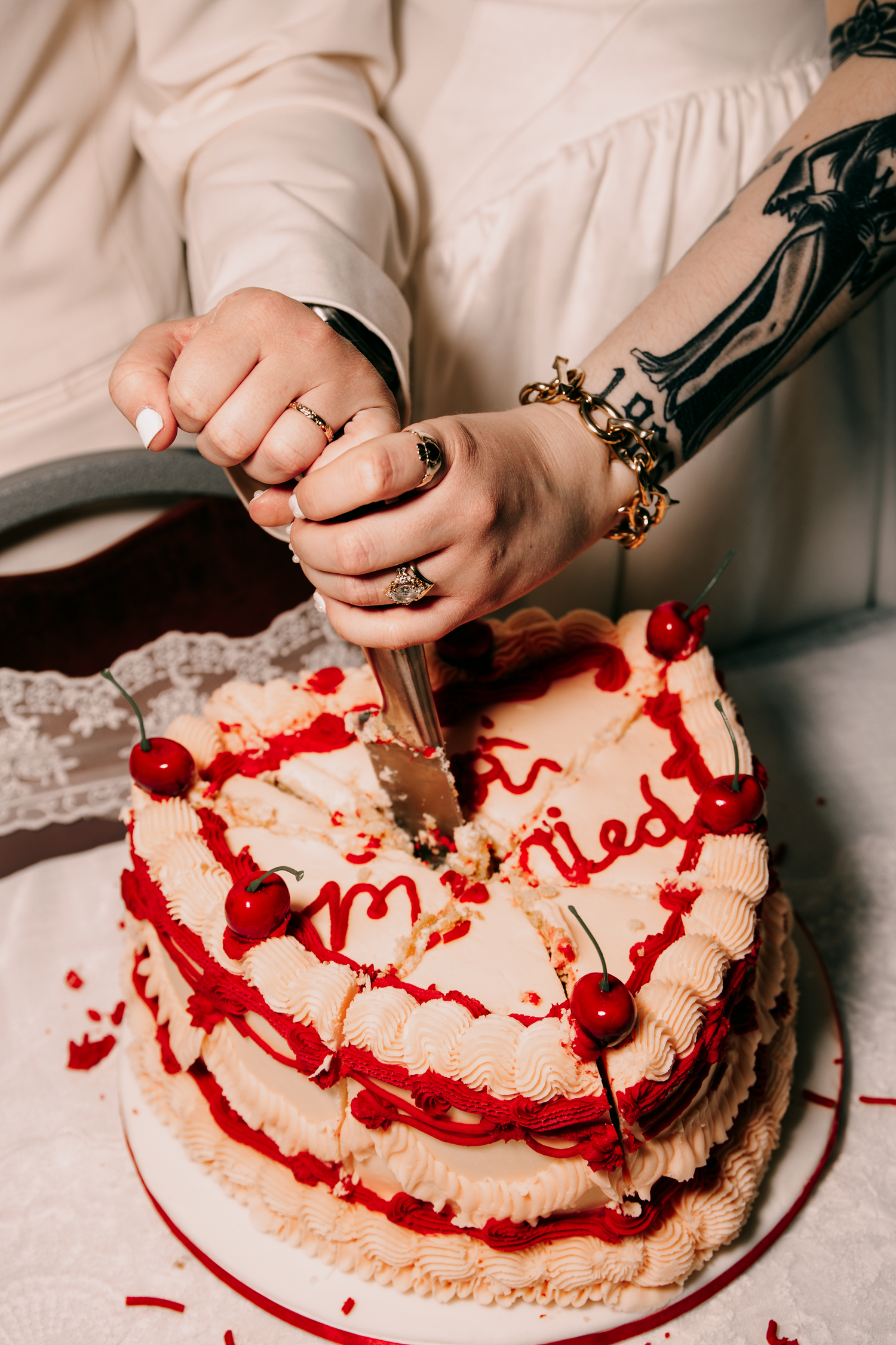Two brides cut a heart-shaped wedding cake decorated with cherries and red frosting together.