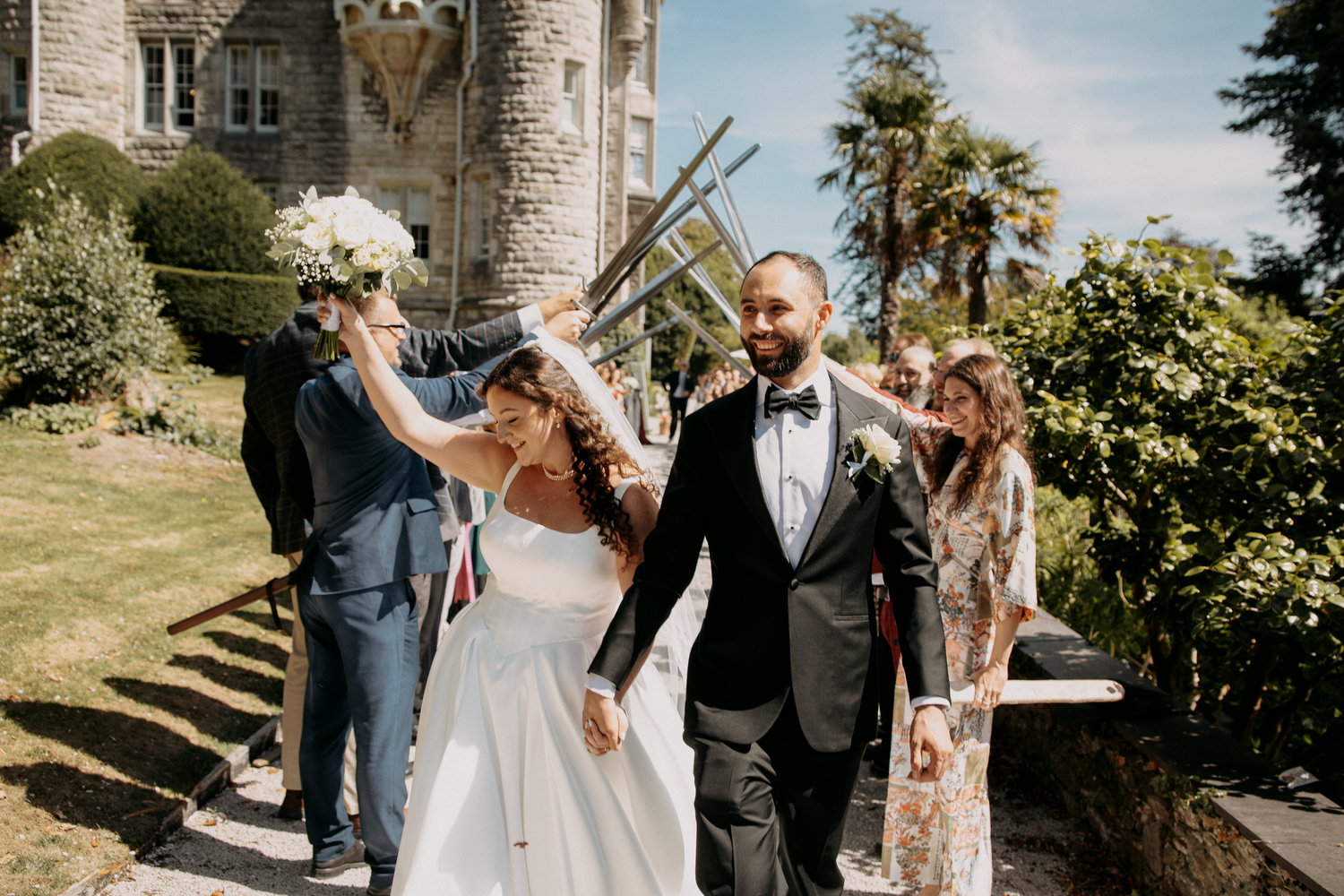 Bride and groom walk joyfully outside a castle venue, surrounded by guests celebrating with sparklers on a sunny wedding day.