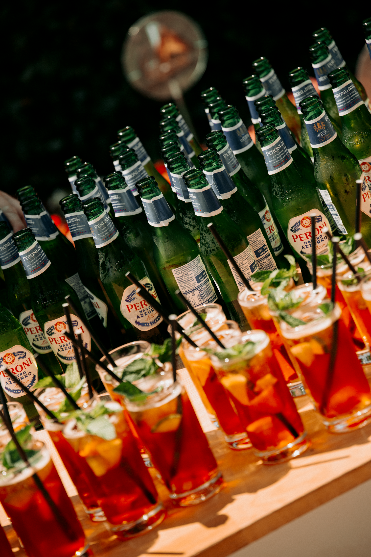 Rows of Peroni beer bottles and Pimms cocktails displayed on a table at a wedding reception.