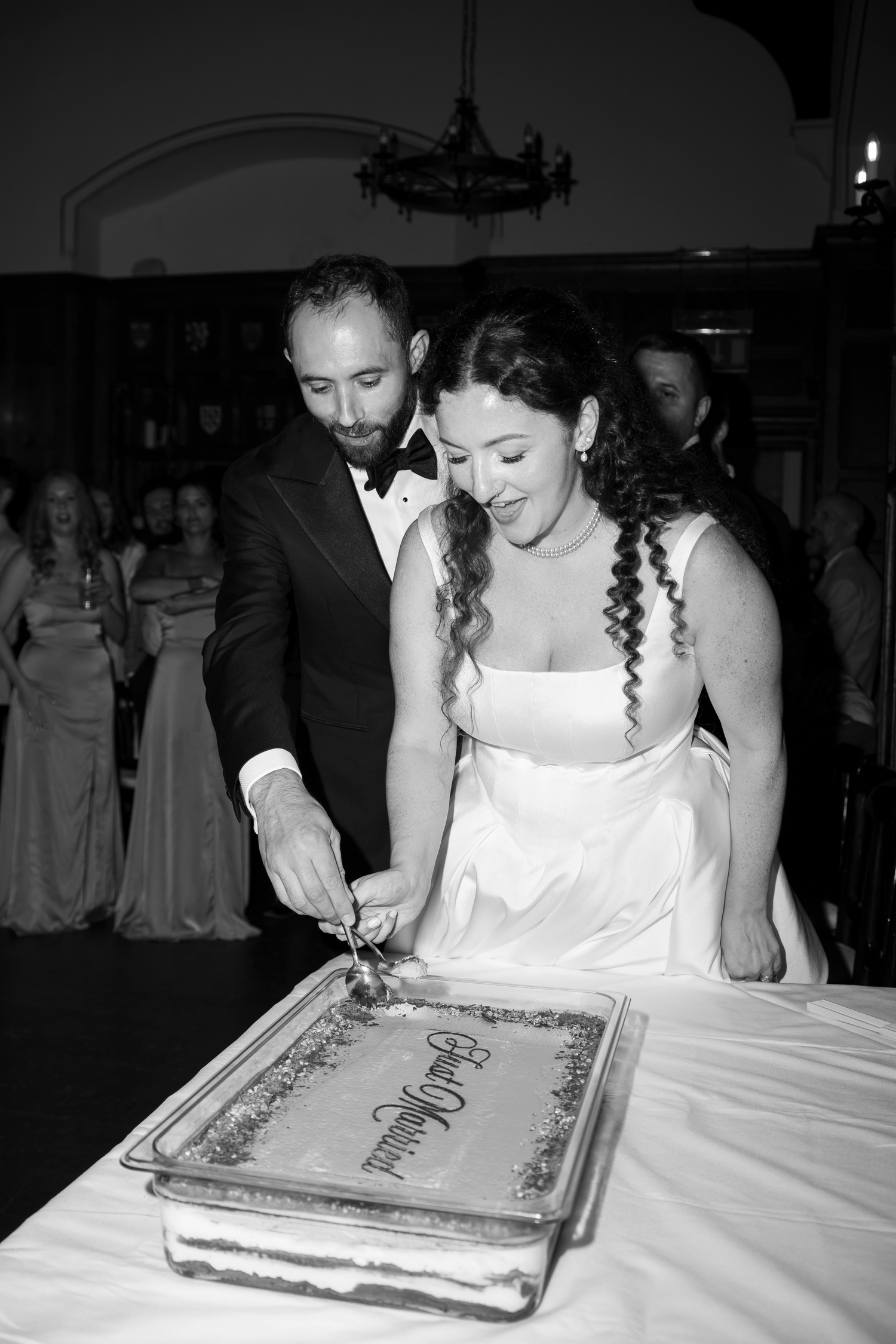 Bride and groom cutting their wedding cake together in black and white photo at elegant reception.