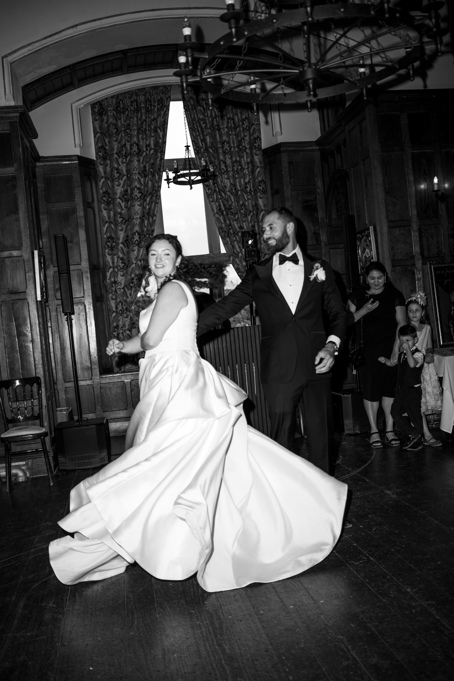 Bride and groom share their first dance in a grand ballroom, captured in elegant black and white wedding photography.