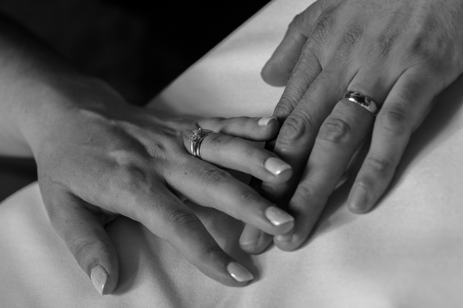 Black and white photo of two hands wearing wedding rings touching gently, symbolizing marriage and love.