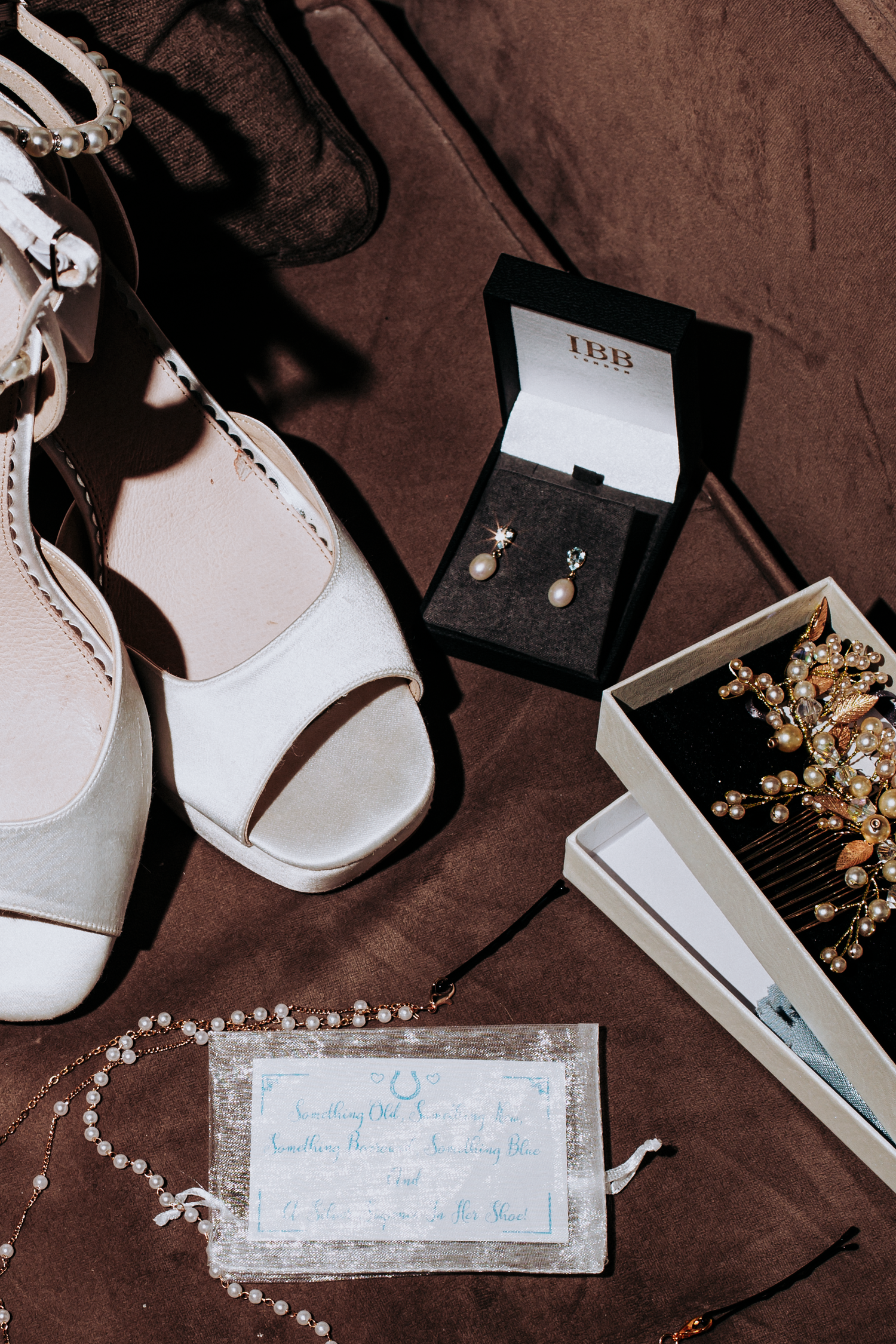 Bridal flat lay featuring white heels, pearl earrings in a jewelry box, gold hair comb, pearl necklace, and wedding day card.