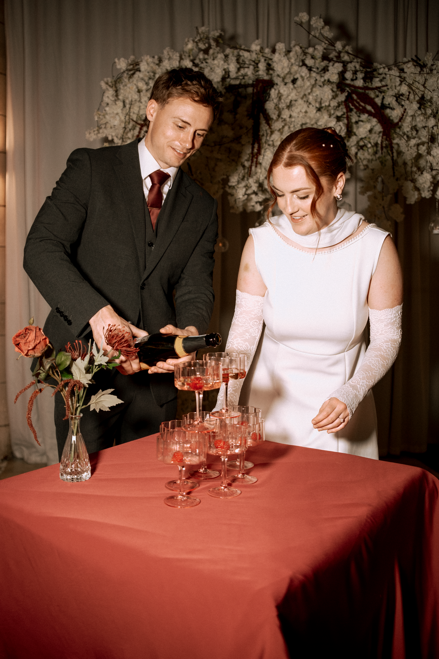 Bride and groom pouring champagne into a pyramid of glasses at wedding.