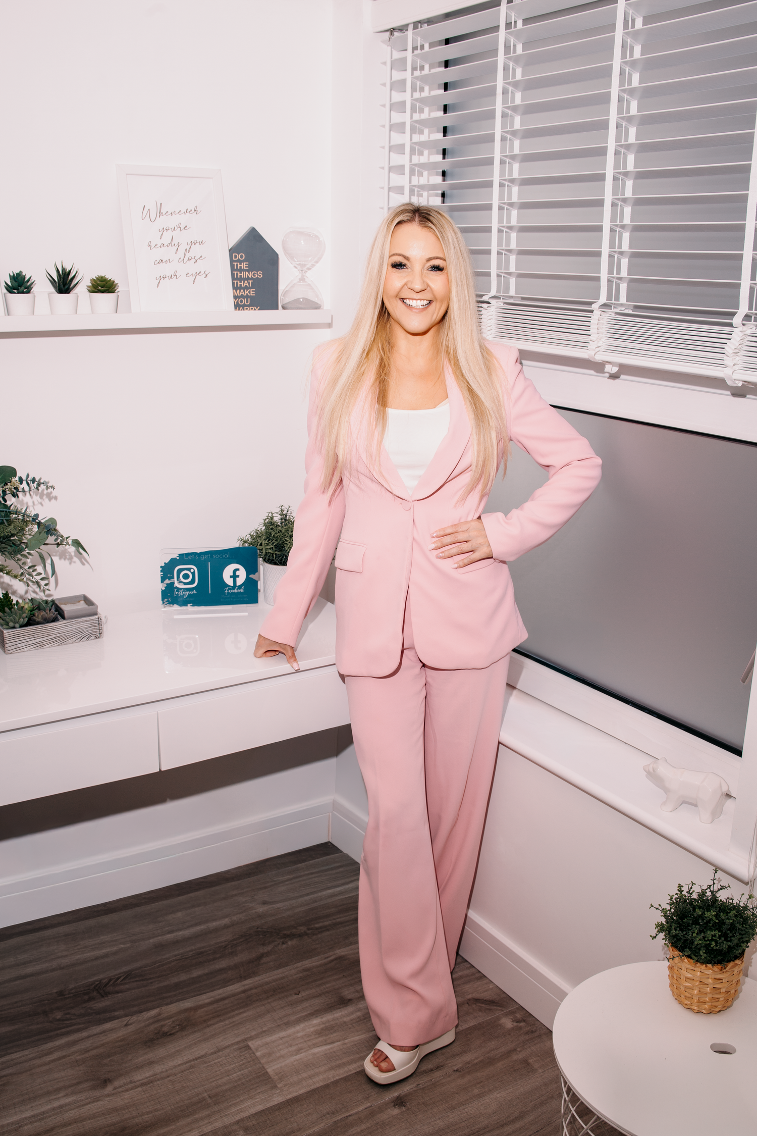 Confident blonde woman in a pink pantsuit standing in a bright professional office space. Hypnotherapy Branding.