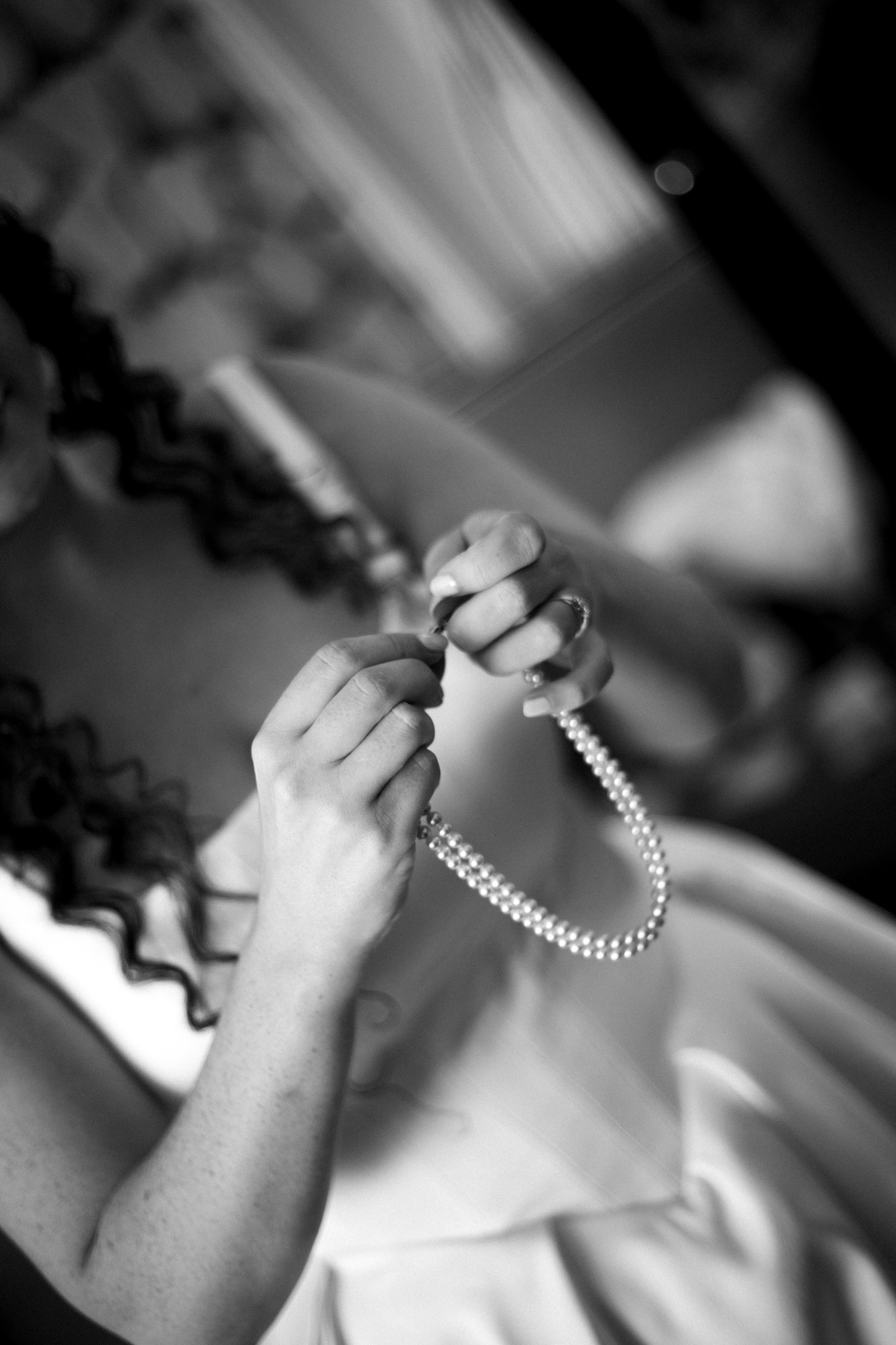 Black and white photo of hands clasping a pearl necklace, bride preparing for wedding ceremony.