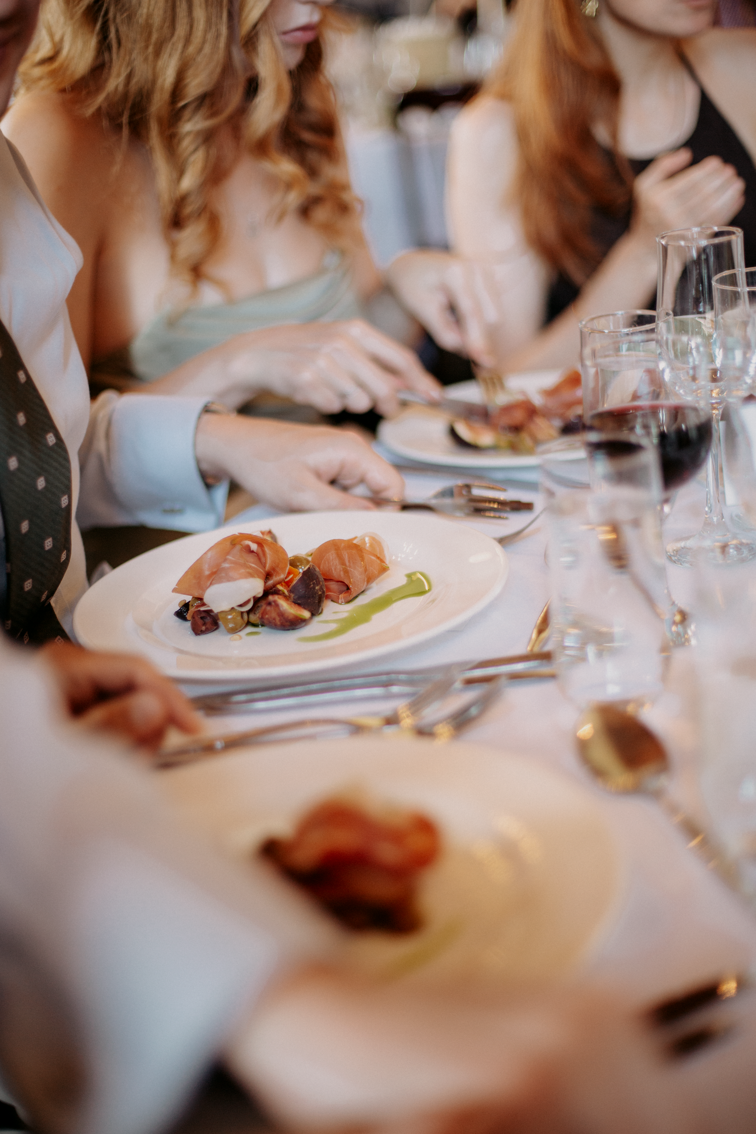 Elegant dinner party table setting with gourmet plated dishes, wine glasses, and guests dining together.