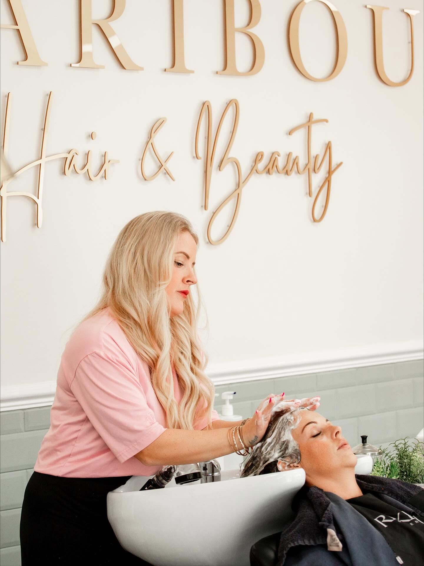 Blonde hairstylist washing a clients hair at a salon basin under a Hair and Beauty sign. Salon Photography.