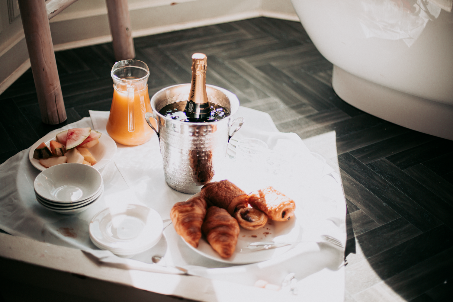 Elegant breakfast tray with croissants, fresh fruit, orange juice, and champagne in ice bucket for a luxury hotel experience.