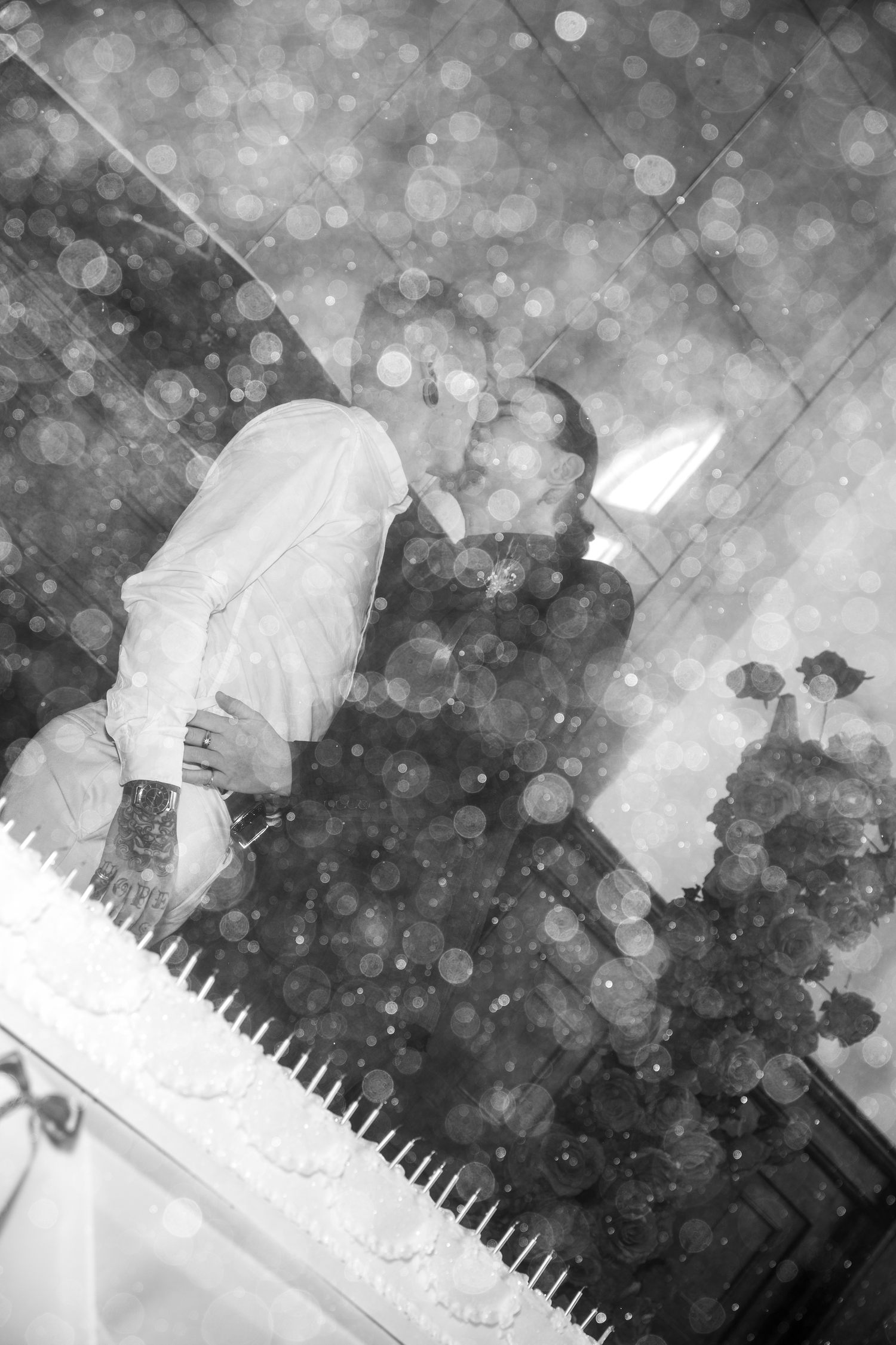 Black and white double exposure photo of couple kissing reflected in wedding cake candles.