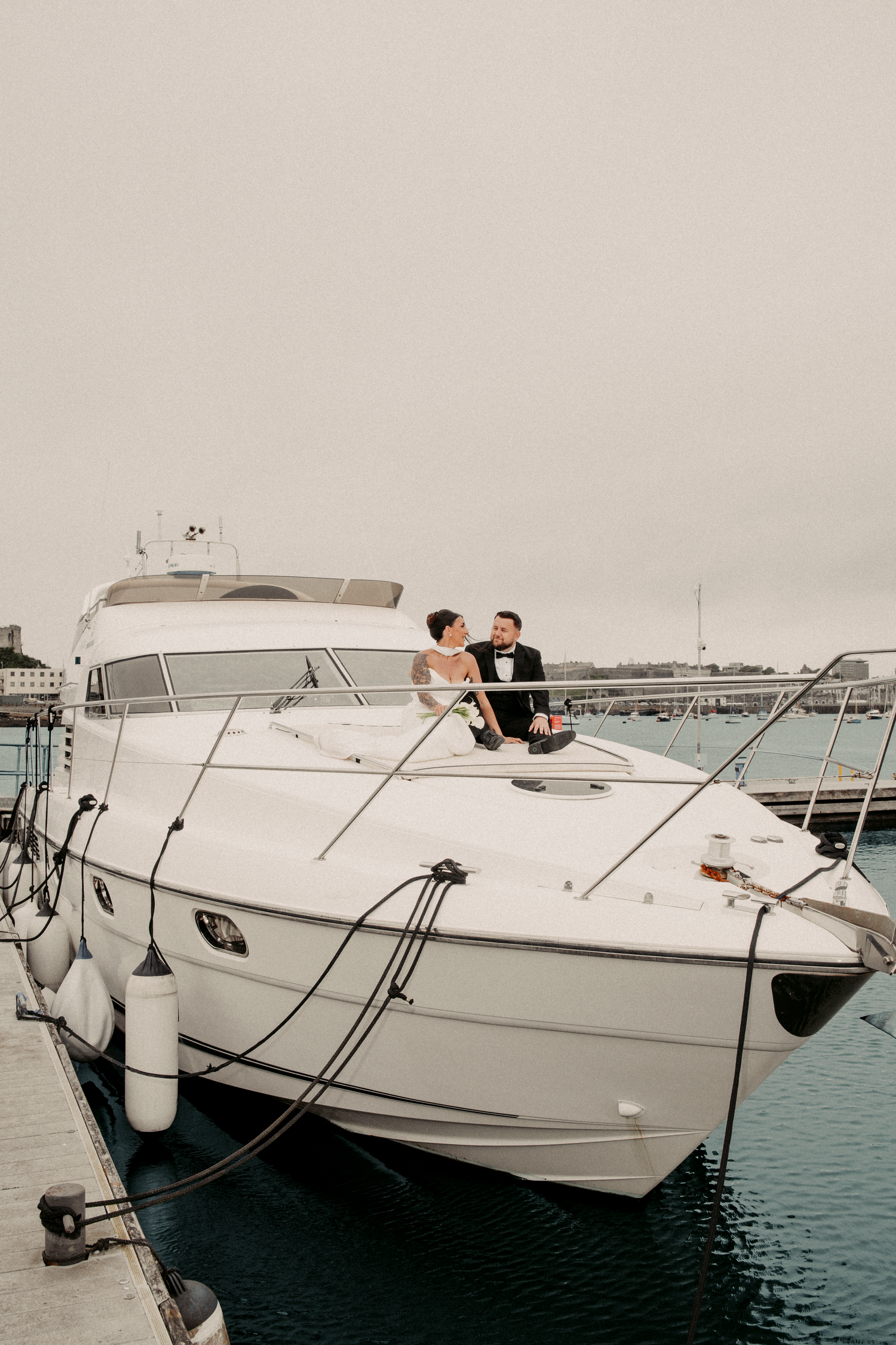 Elegant bride and groom sitting together on a luxury white yacht docked in a marina.