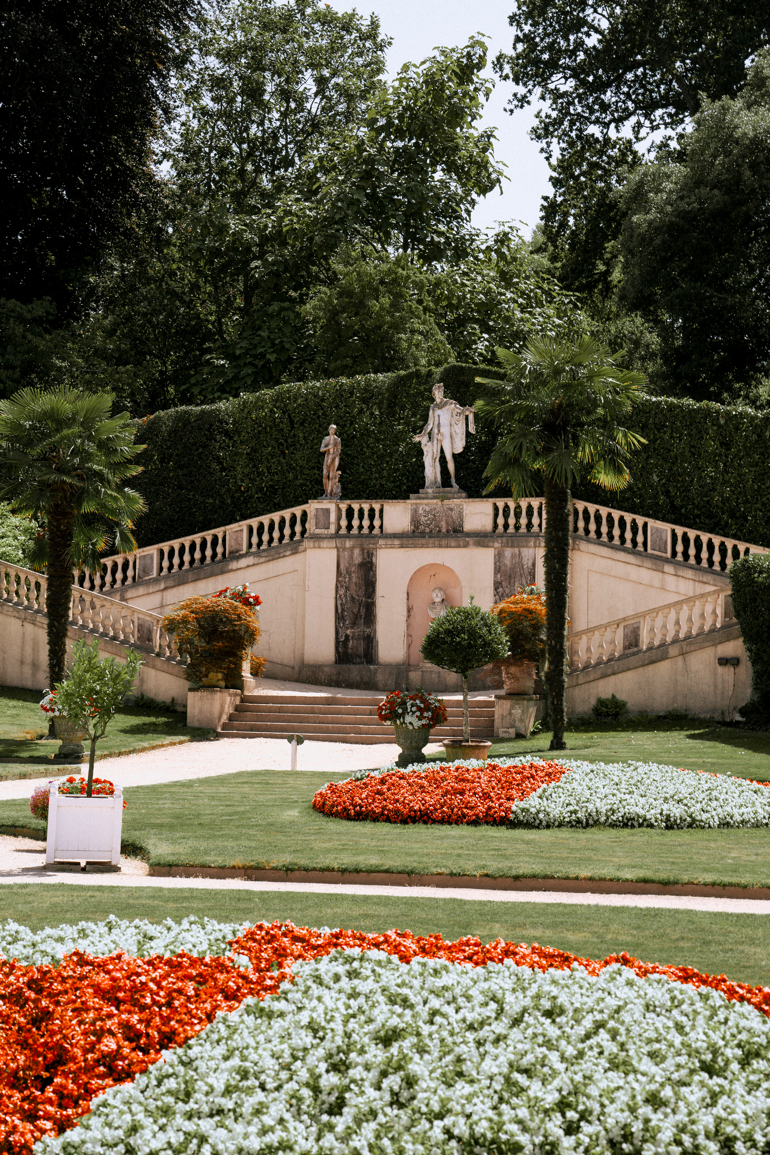 Elegant Italian garden with colorful flower beds, statues, balustrade staircase, and lush greenery.