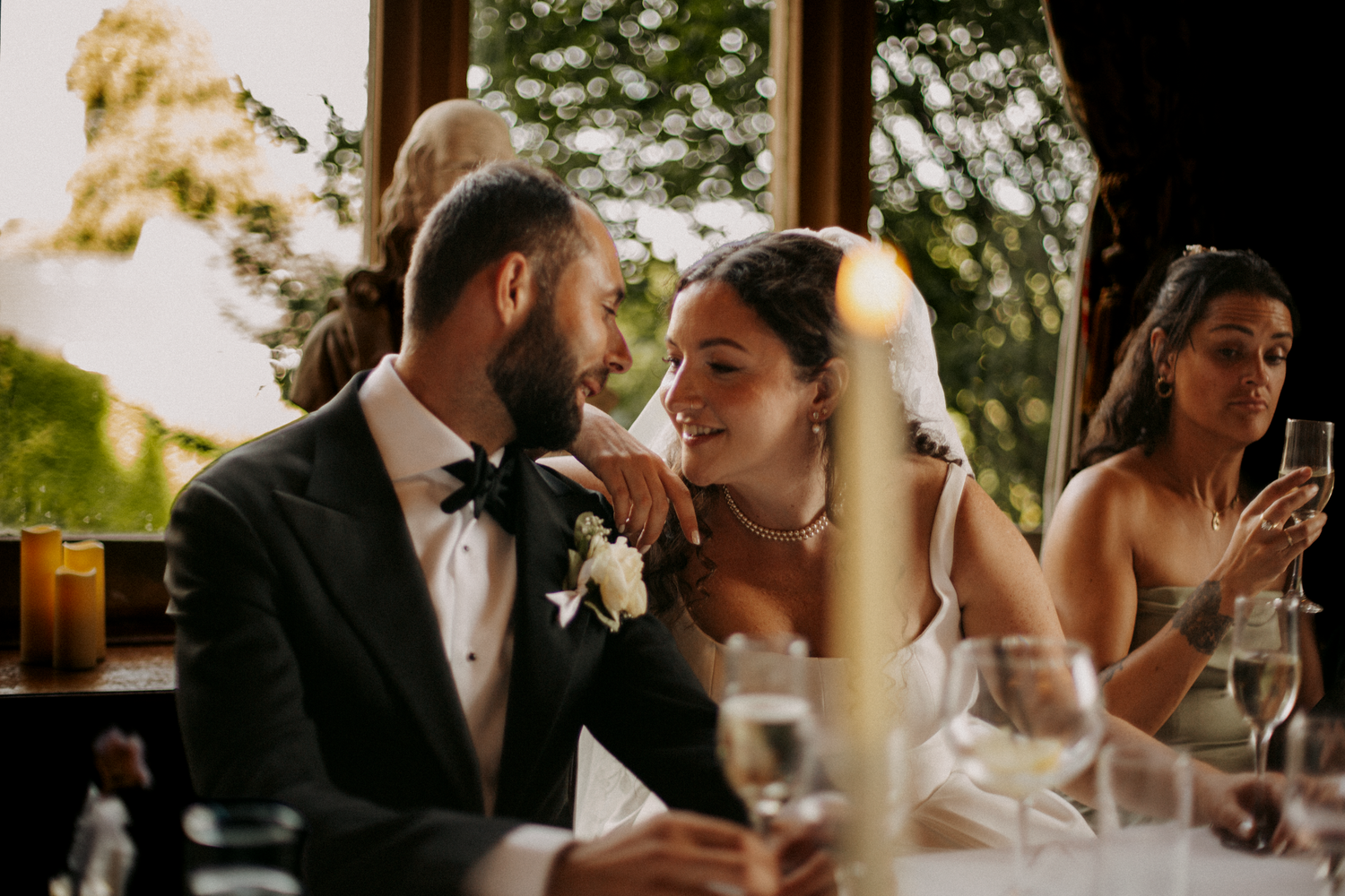 A bride and groom share a tender moment at their wedding reception dinner table, smiling at each other.