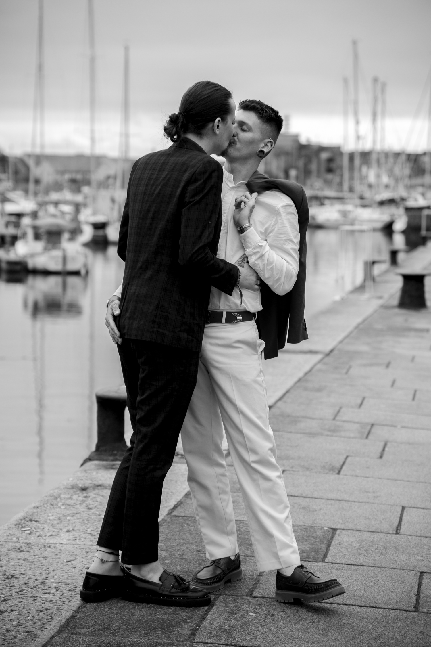 Two grooms share a romantic kiss on a harbor waterfront in black and white wedding photography.