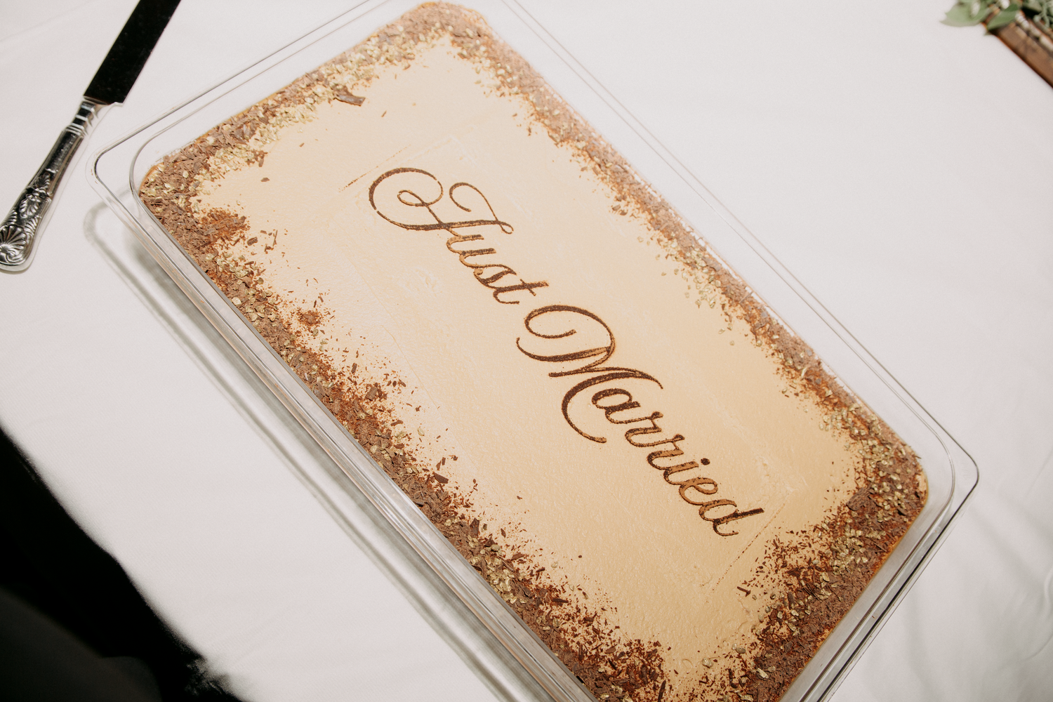 Just Married tiramisu wedding cake with elegant script lettering on a white tablecloth at a reception.