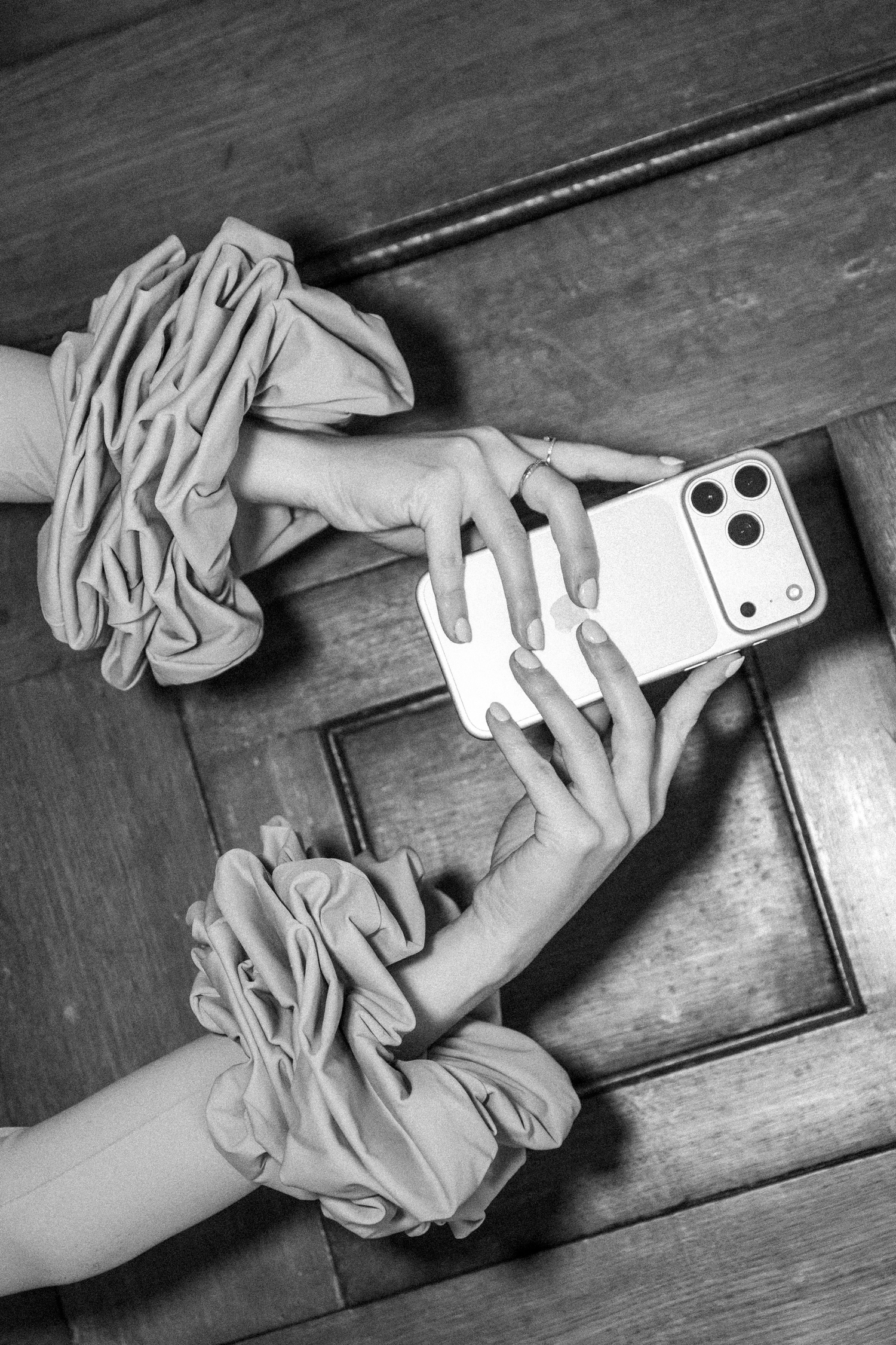 Black and white photo of hands with ruffled sleeves holding a modern smartphone on a wooden floor. Content Creator Branding Shoot