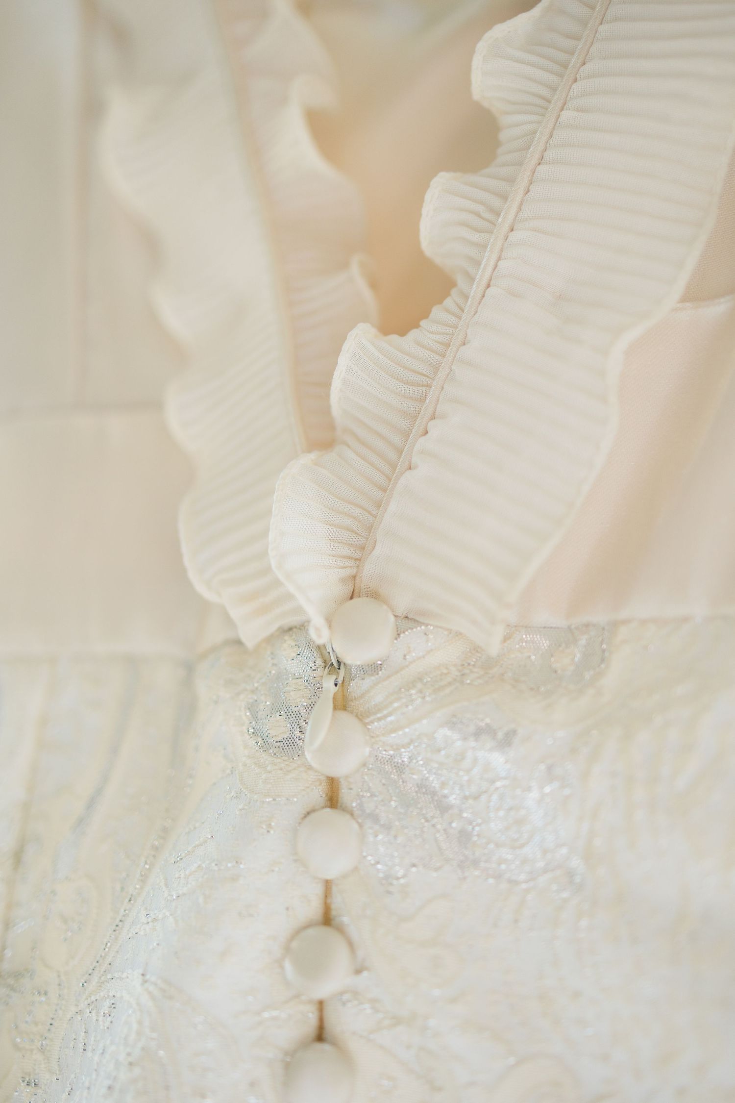 Close-up of elegant white wedding dress featuring ruffled trim, fabric-covered buttons, and delicate lace detailing.