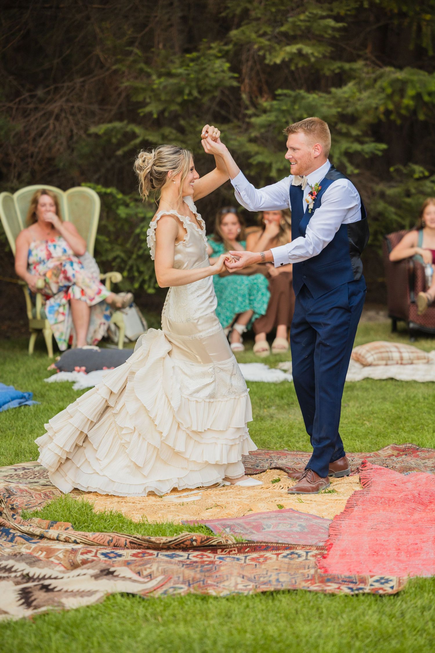 Bride and groom share first dance on colorful rugs at outdoor boho wedding surrounded by seated guests.