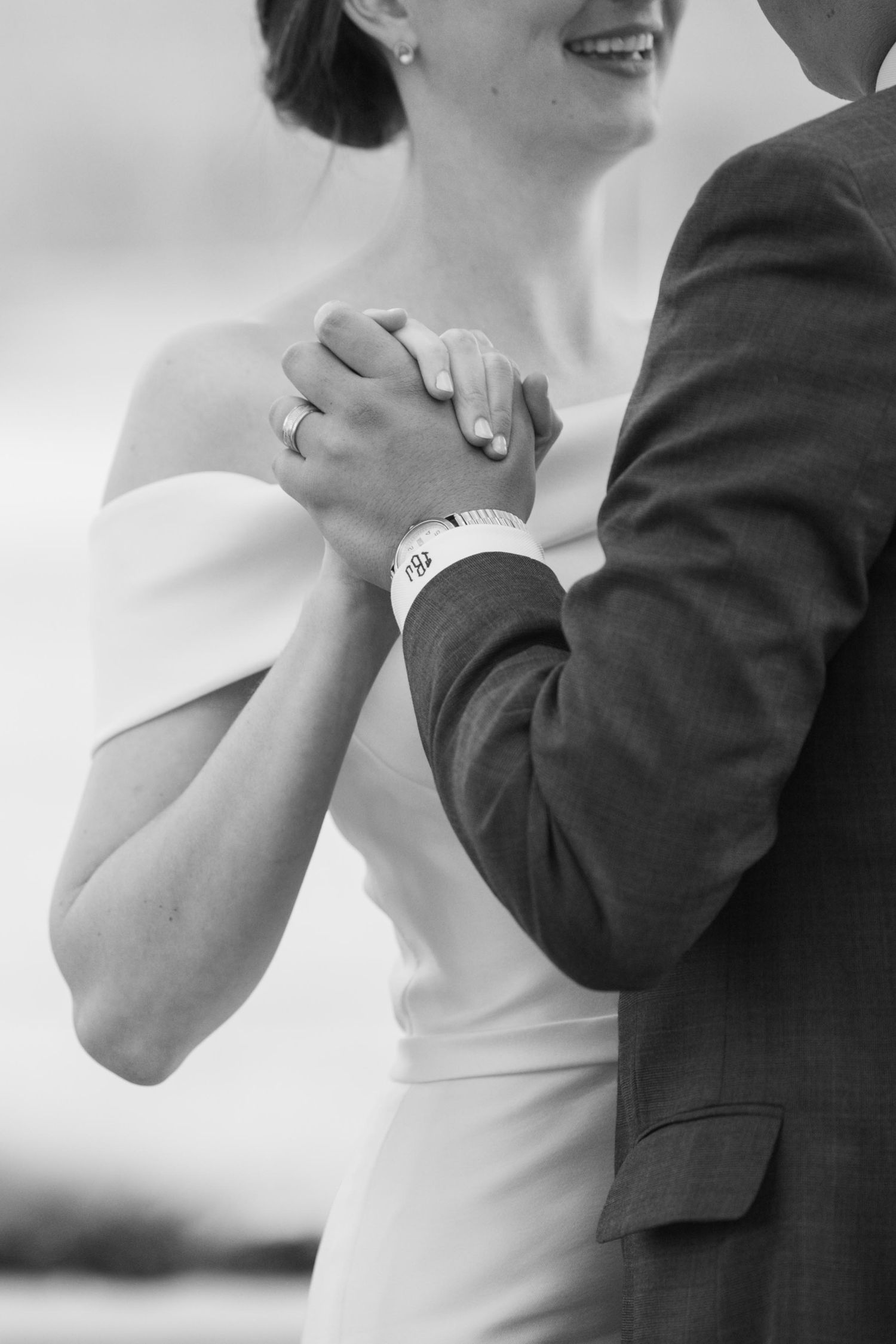 Black and white photo of a bride and groom holding hands closely during their first dance.