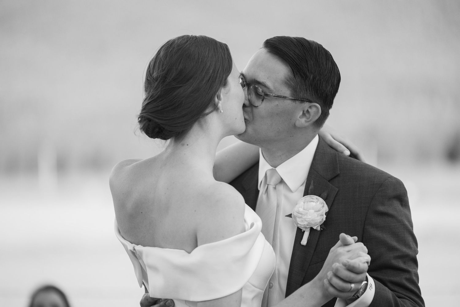 Black and white photo of bride and groom sharing first dance kiss at wedding reception.