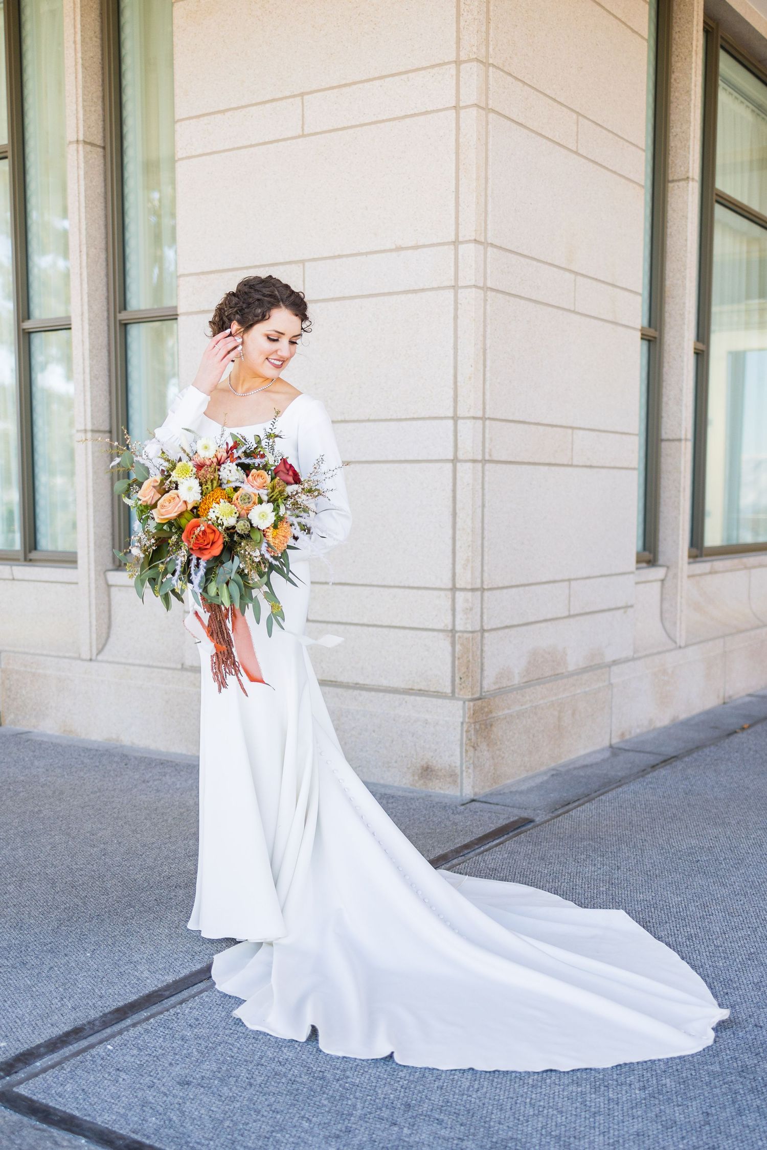 Bride in white gown holding colorful bouquet outdoors.
