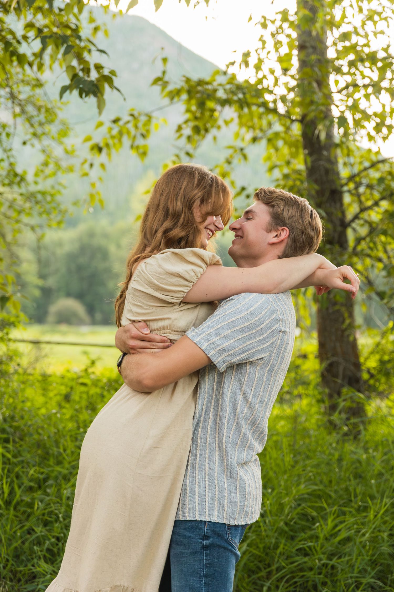 Happy couple embraces and laughs together in lush green mountain meadow during outdoor photo session.
