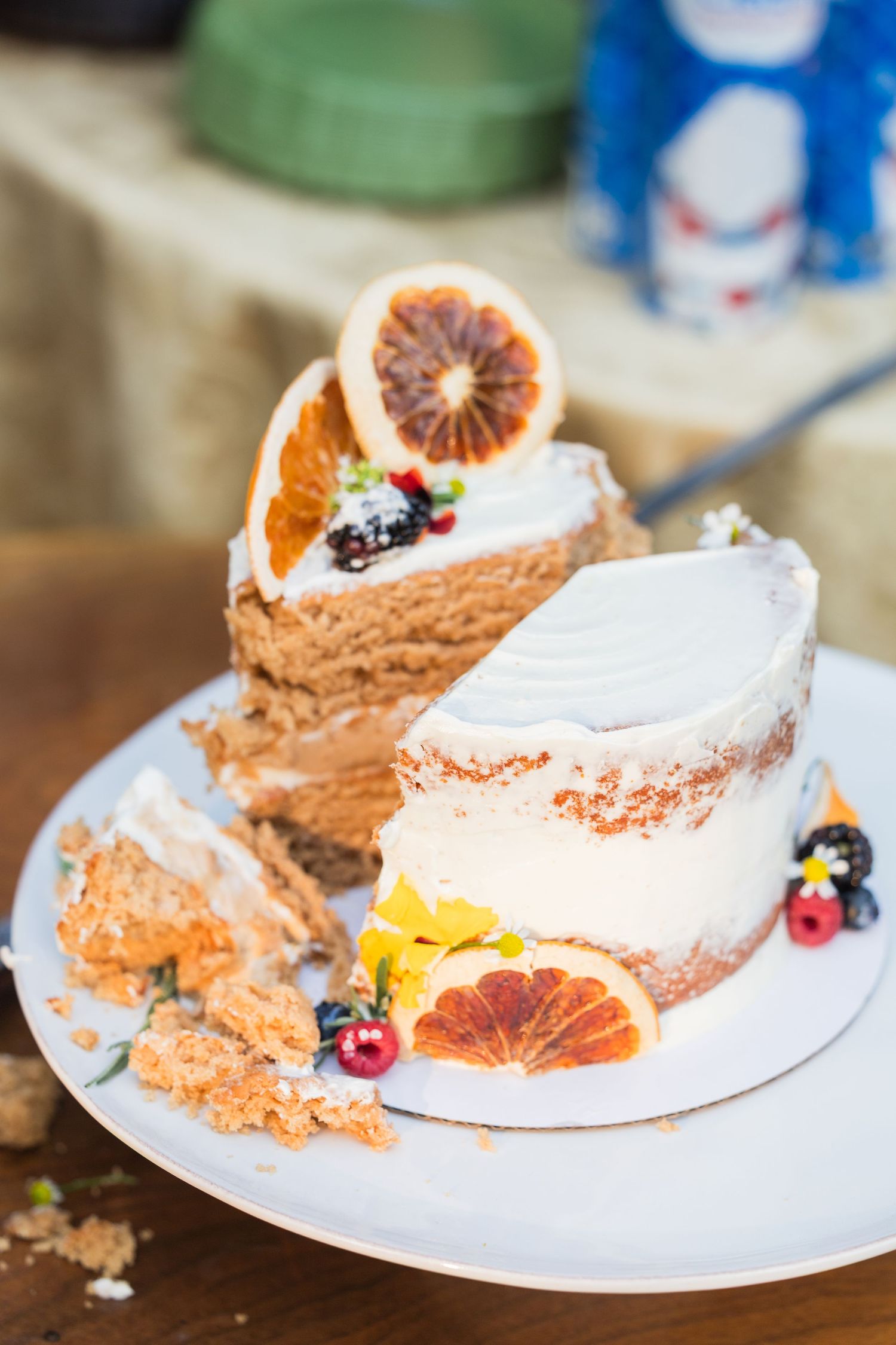 Partially sliced naked wedding cake decorated with blood oranges and berries on white plate.