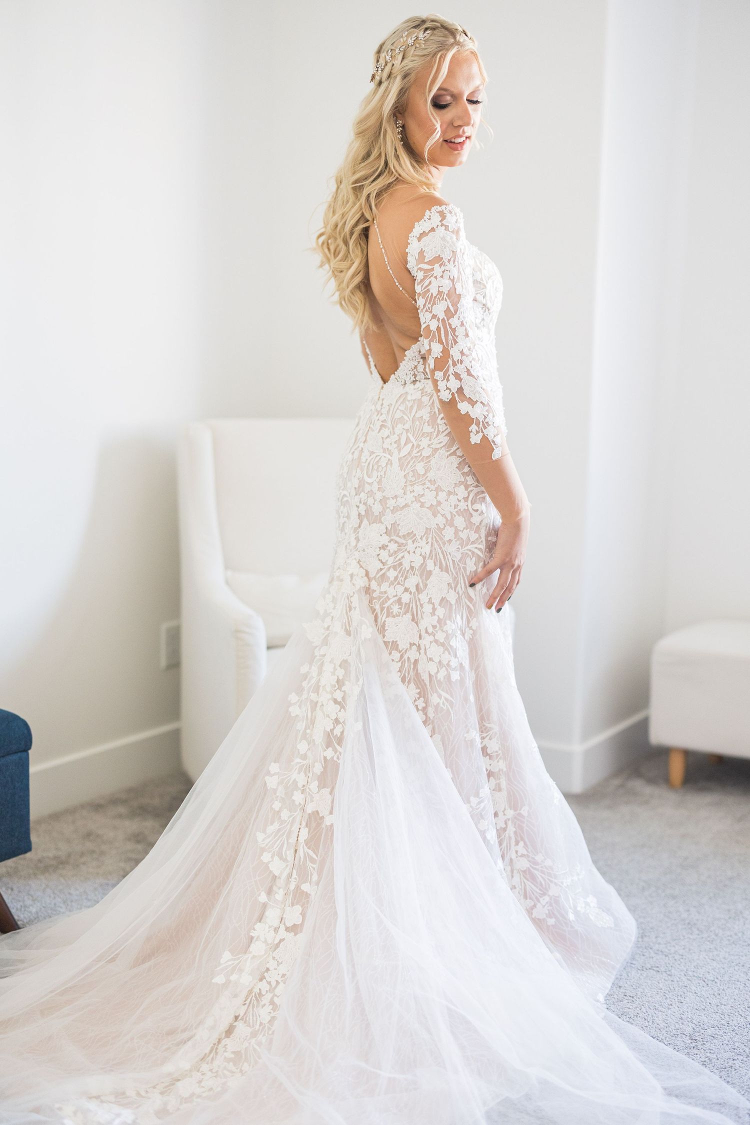 Bride in elegant backless lace wedding gown with floral appliques and train poses in bright room.