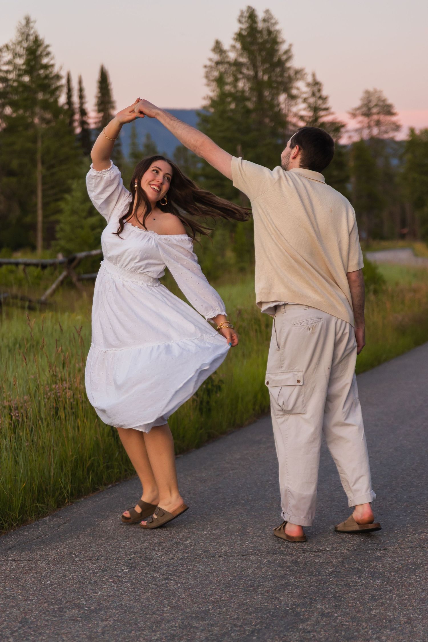 Couple dancing on a road at sunset surrounded by lush green trees and mountains.