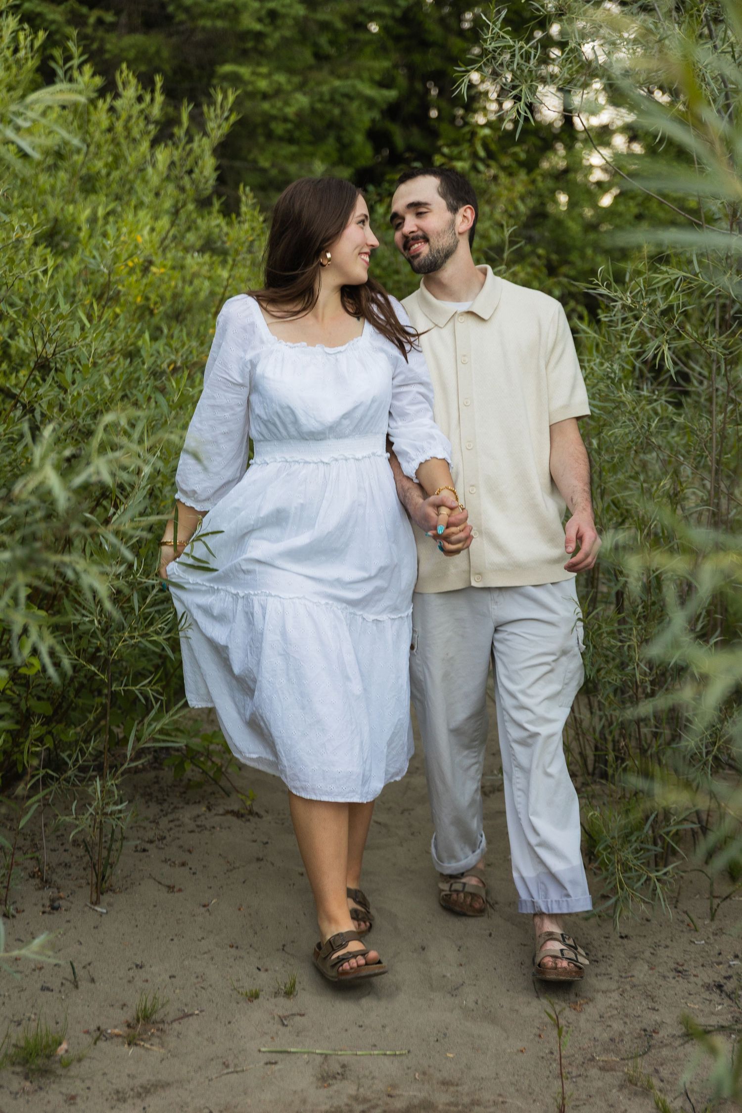 Happy couple walking hand in hand through lush green sandy nature path together.