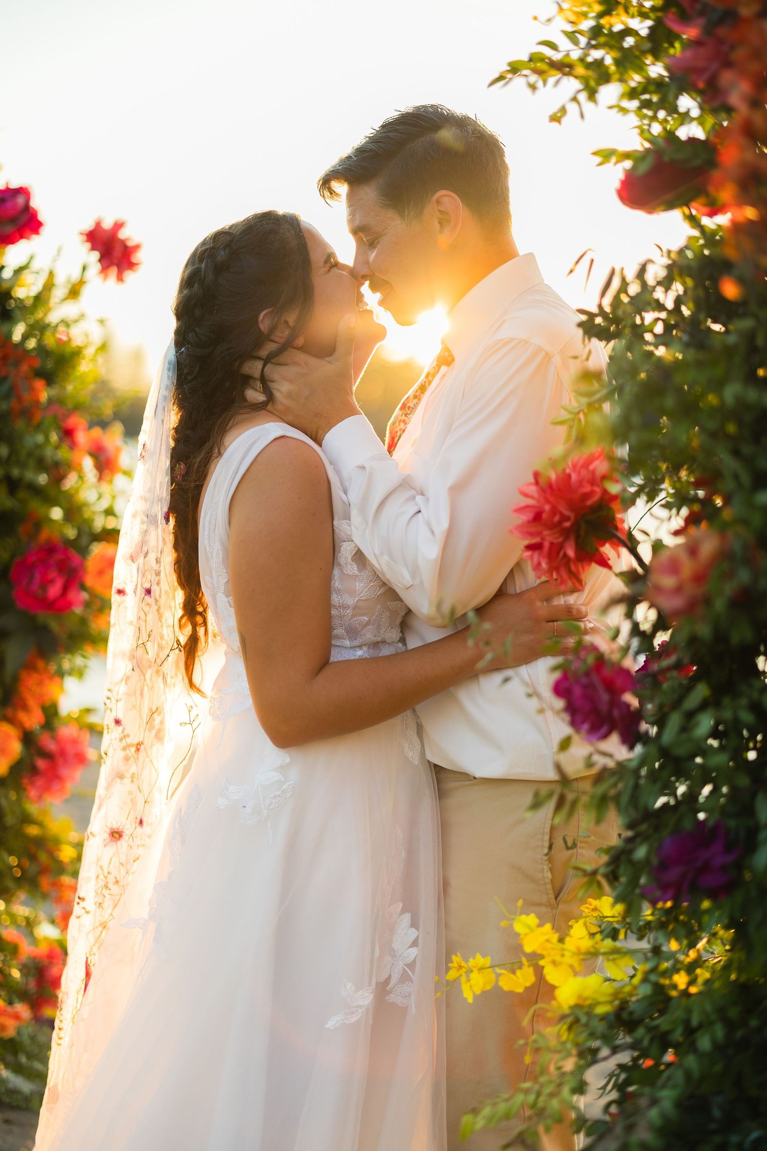 Couple kissing at sunset surrounded by colorful flowers.
