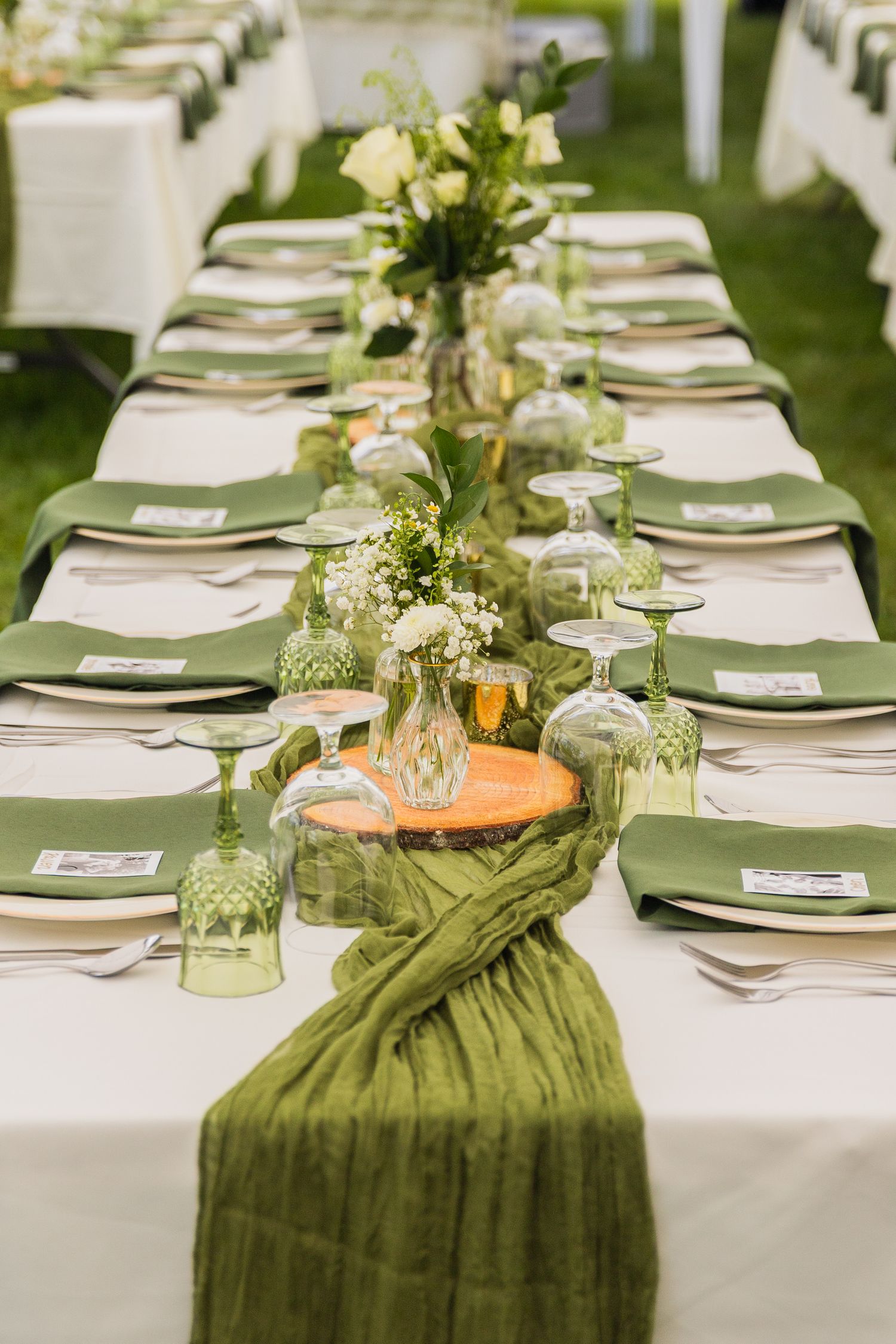 Long wedding reception table with green runners, wood slice centerpieces, and elegant white floral arrangements.