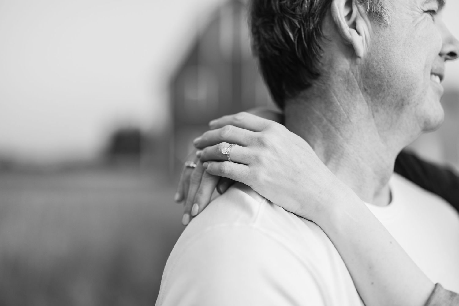 Black and white close-up of a woman placing her hand on a mans shoulder showing an engagement ring.