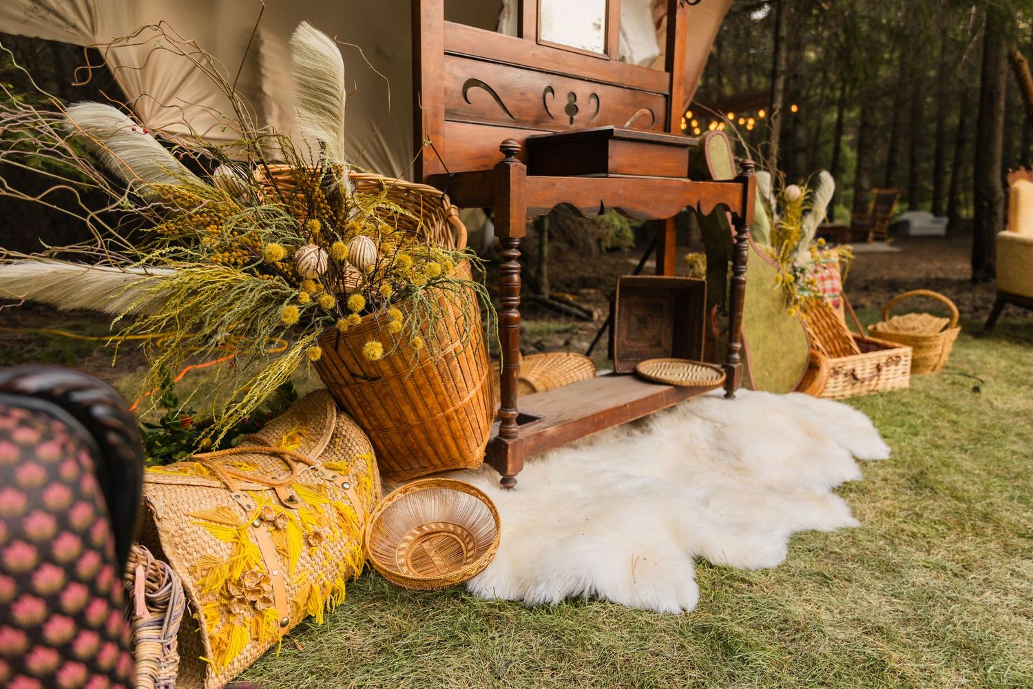 Rustic outdoor boho wedding decor with wicker baskets, floral arrangements, and sheepskin rug on grass.